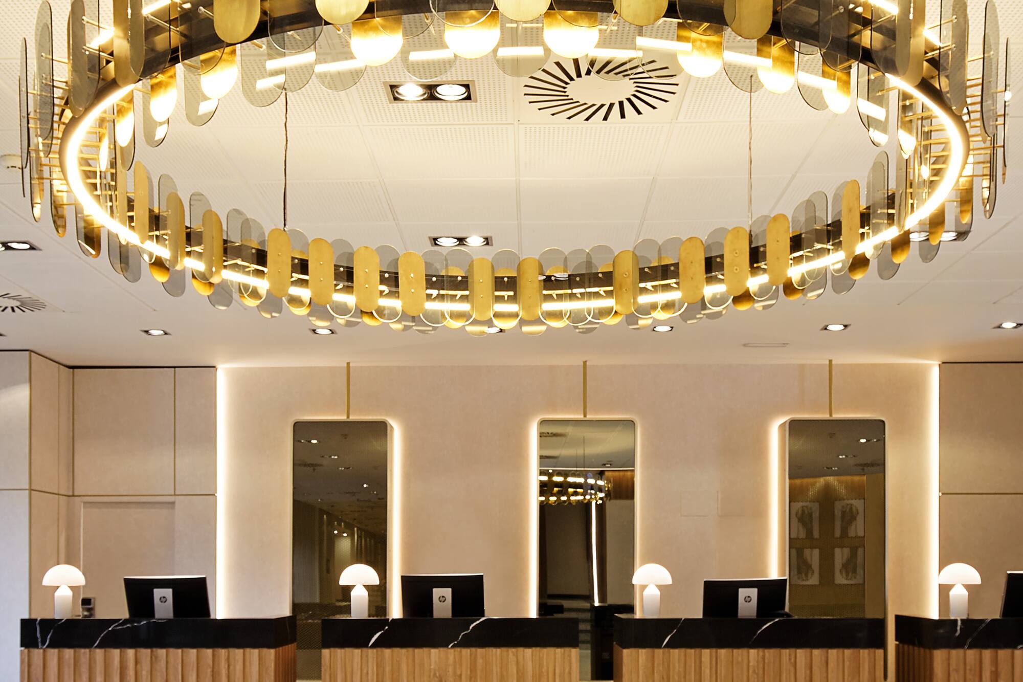 Modern hotel reception with circular gold chandelier and wood front desks.