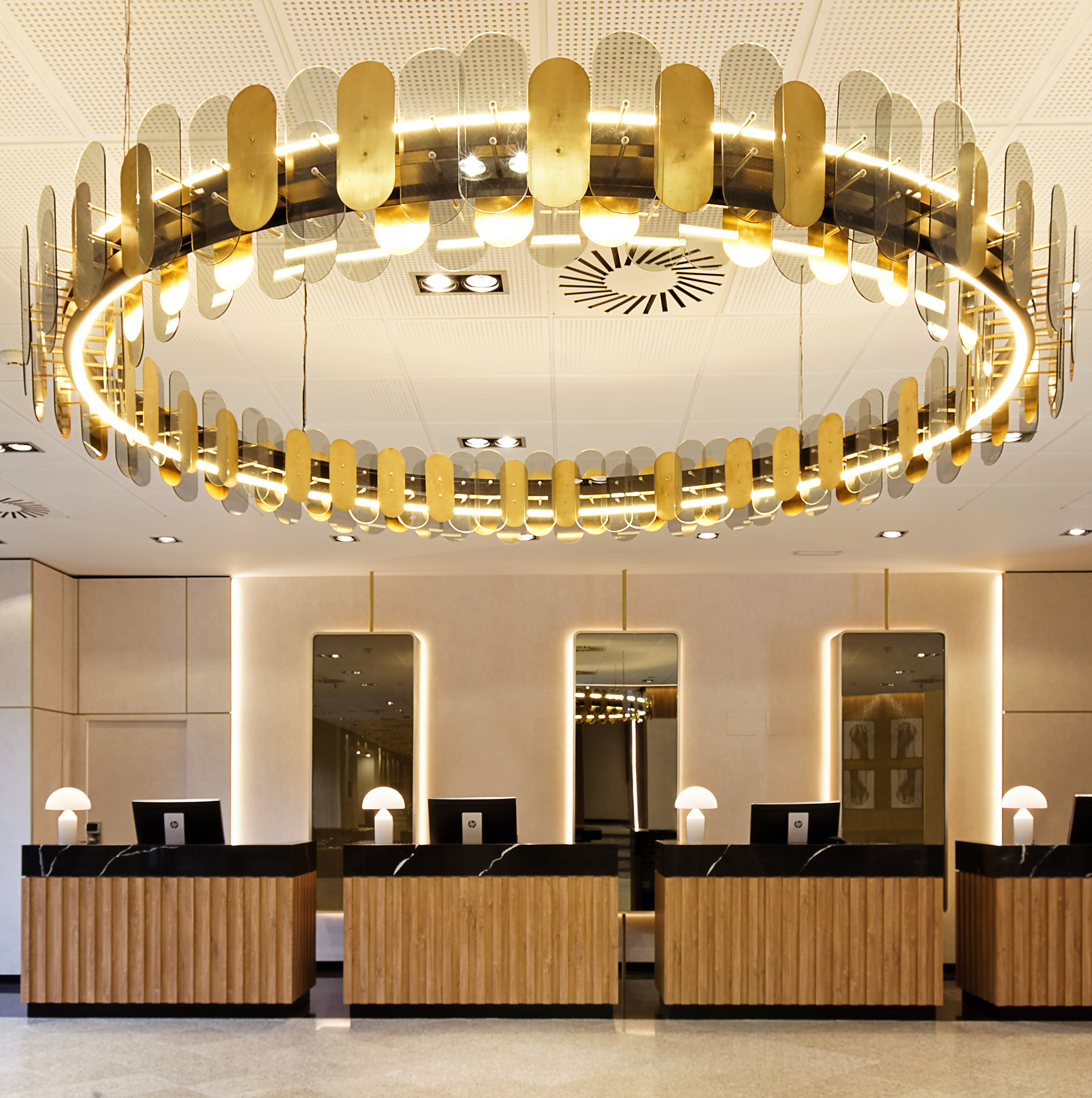 Modern hotel reception with circular gold chandelier and wood front desks.