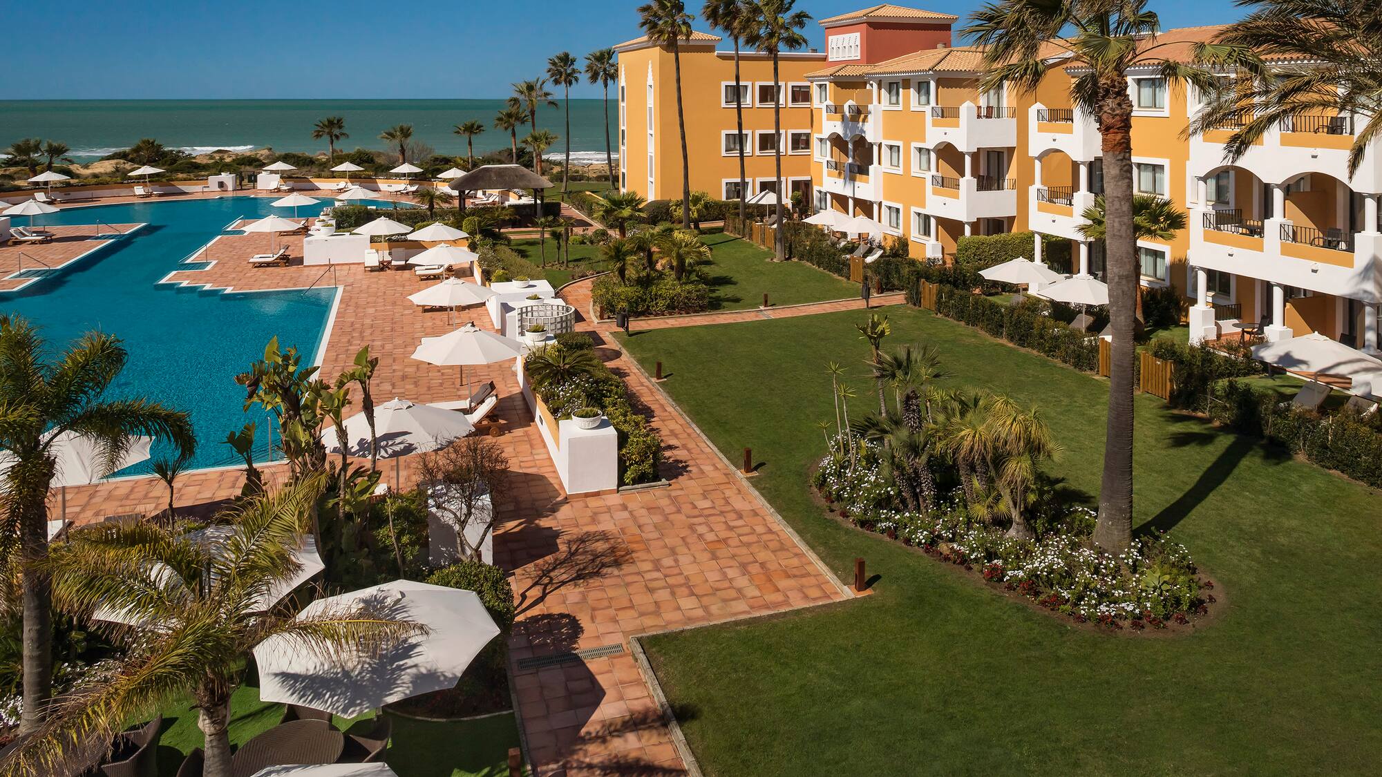 a pool and buildings with palm trees and umbrellas