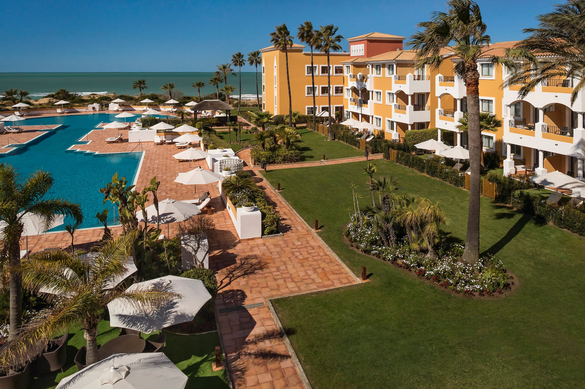a pool and buildings with palm trees and umbrellas