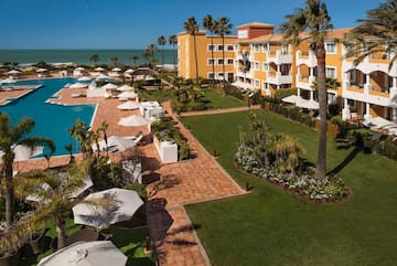 a pool and buildings with palm trees and umbrellas