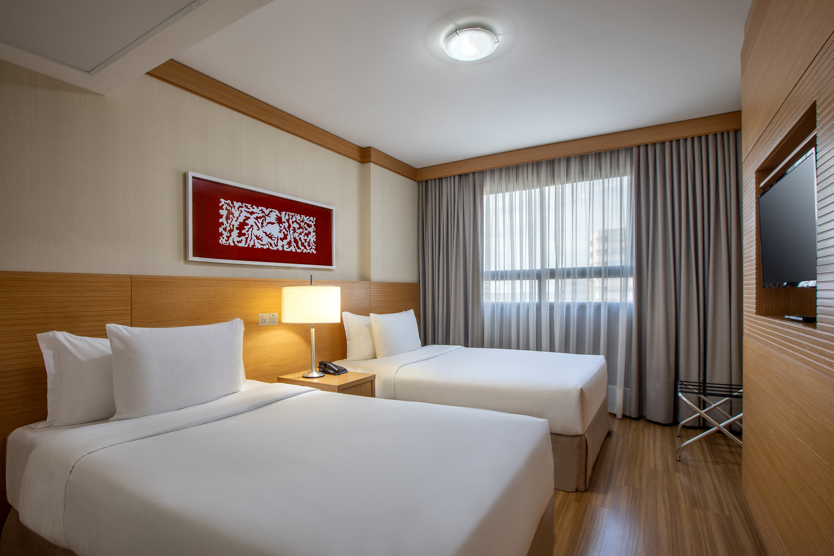 Modern hotel room with two twin beds, white bedding, and wooden accents.