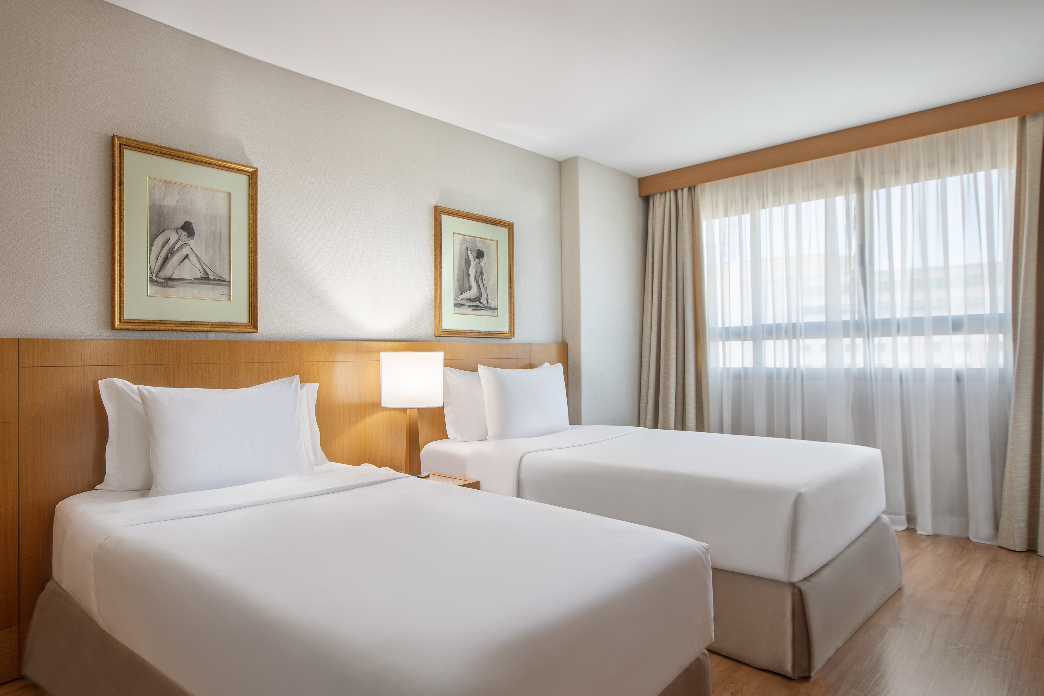 Hotel room with two twin beds, white bedding, wooden headboard, and window.