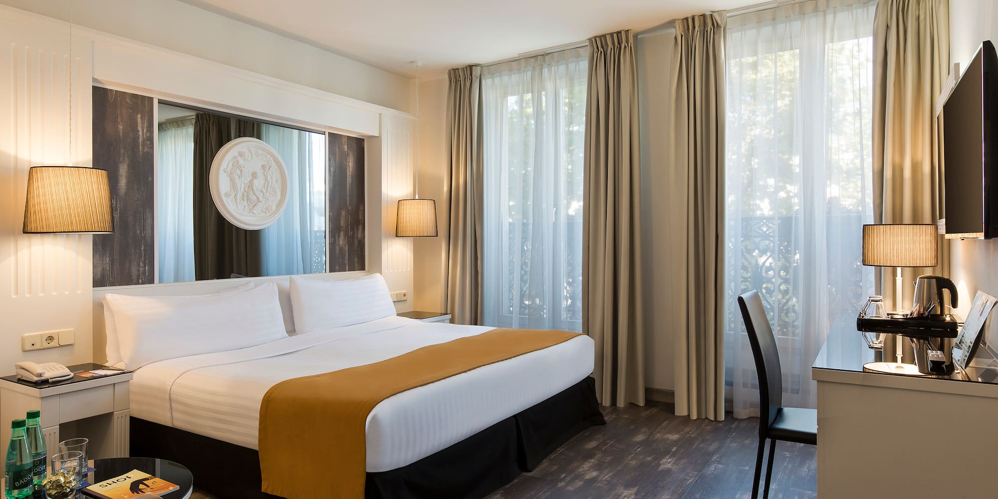 Elegant hotel guest room with king bed, desk, and sunlit windows.