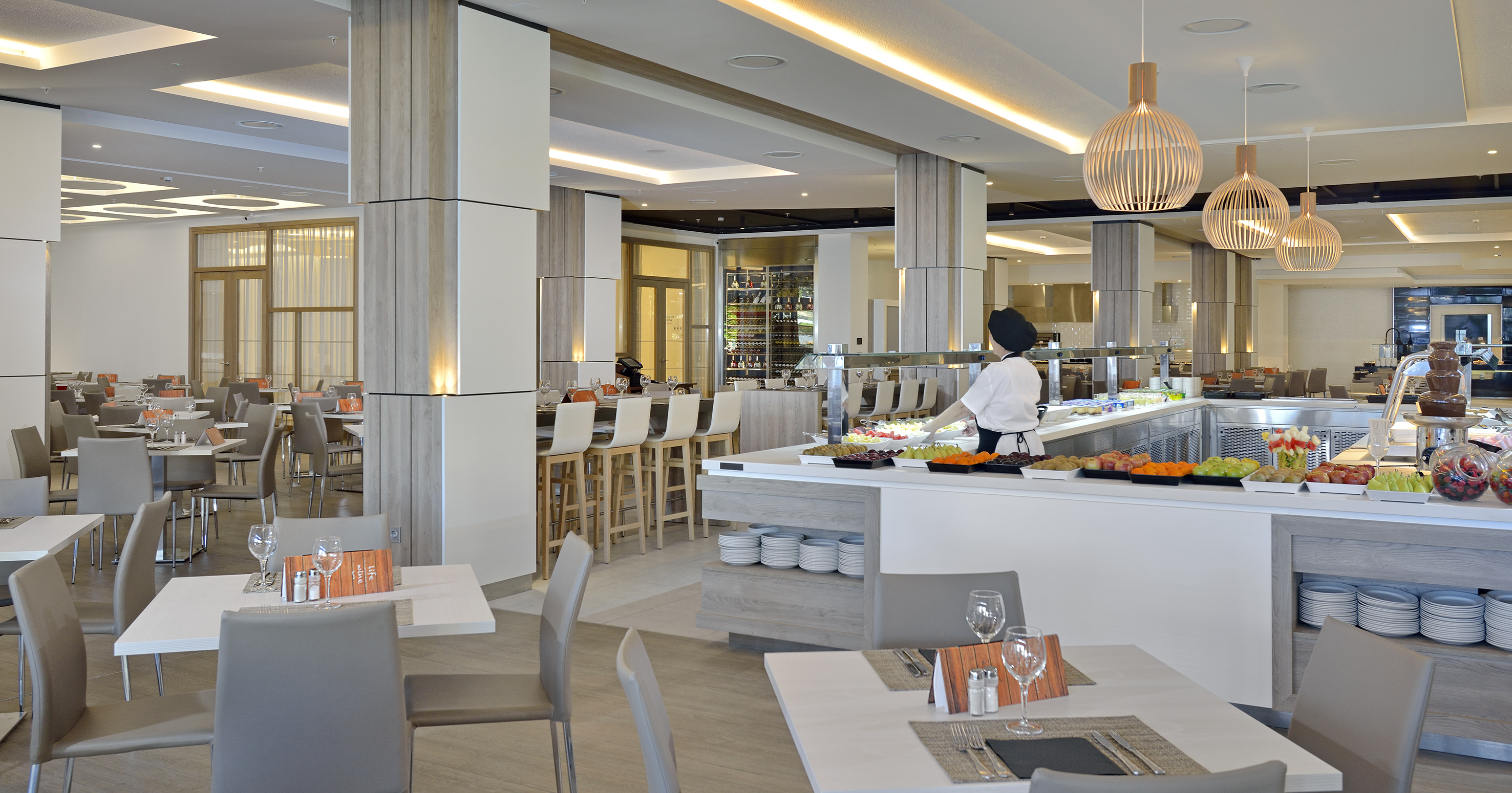Modern hotel restaurant buffet with chef, fresh fruit, and chocolate fountain.
