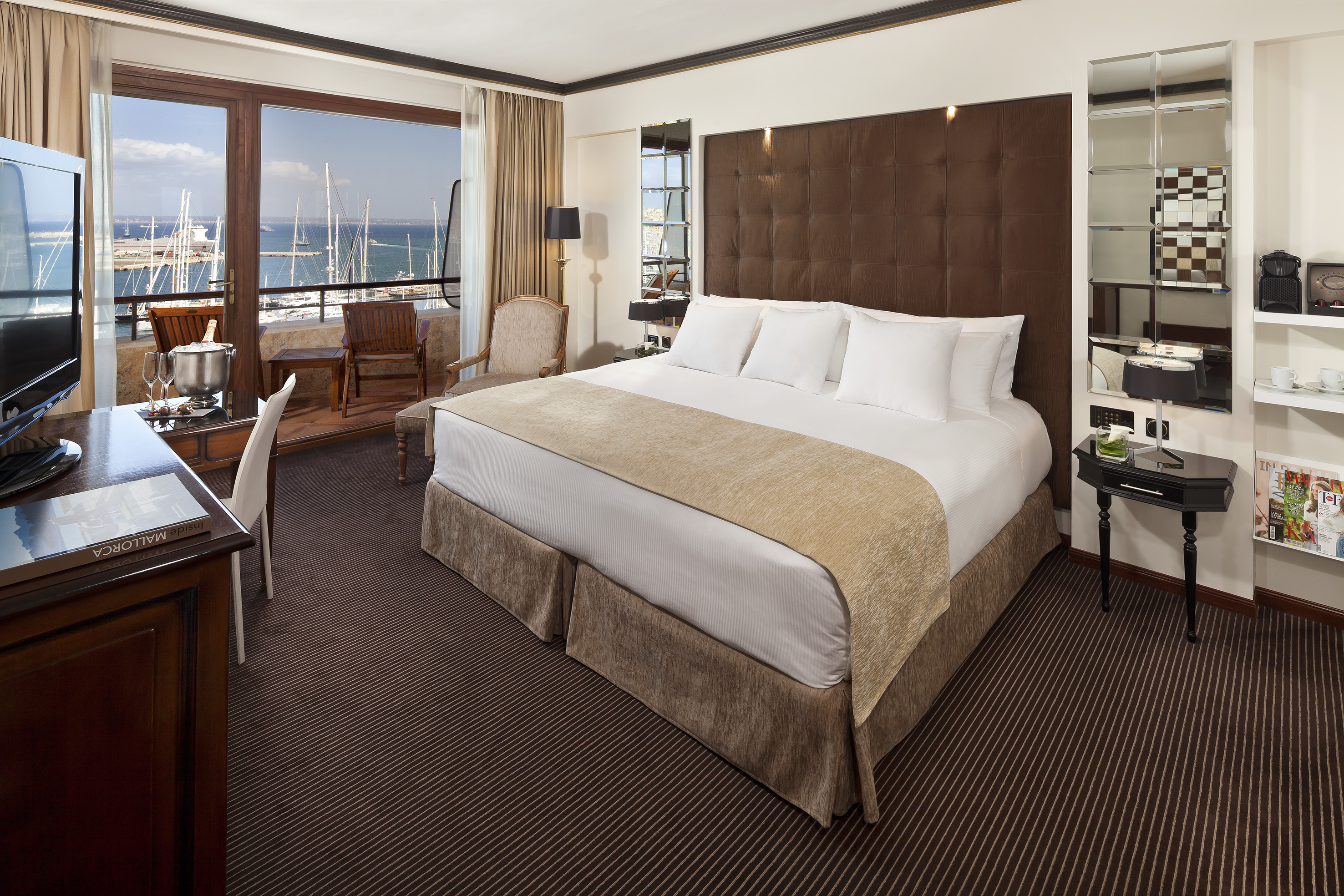 Luxury hotel bedroom with sea view balcony overlooking a marina with yachts.