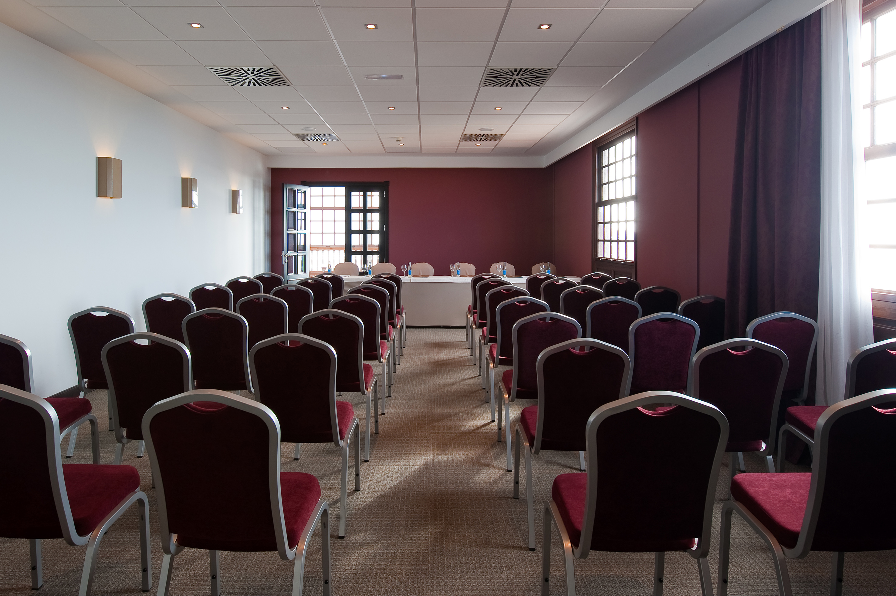 Empty conference room with rows of maroon chairs and a presentation table.