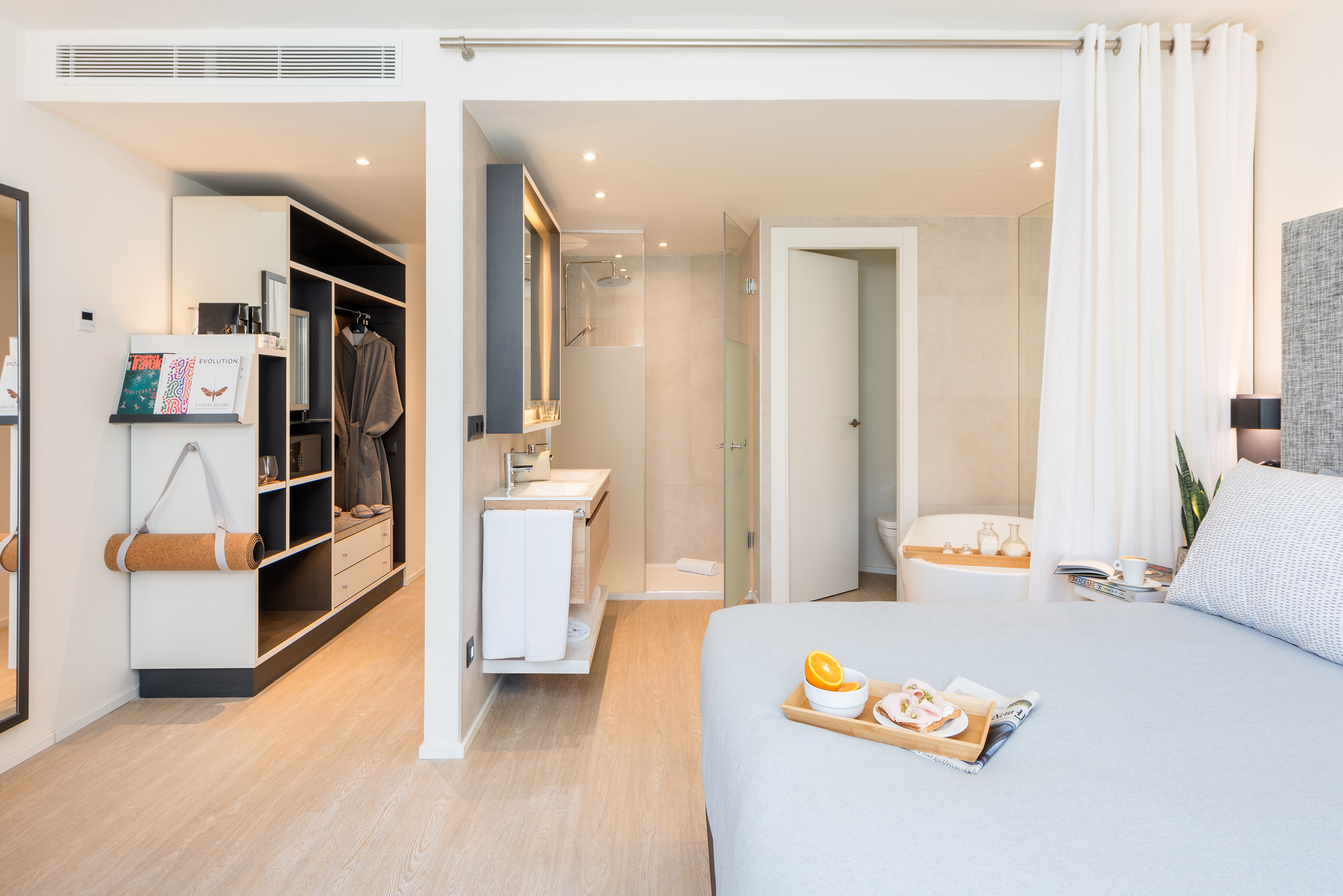 Modern open-plan hotel suite with bedroom, bathroom, and walk-in closet.