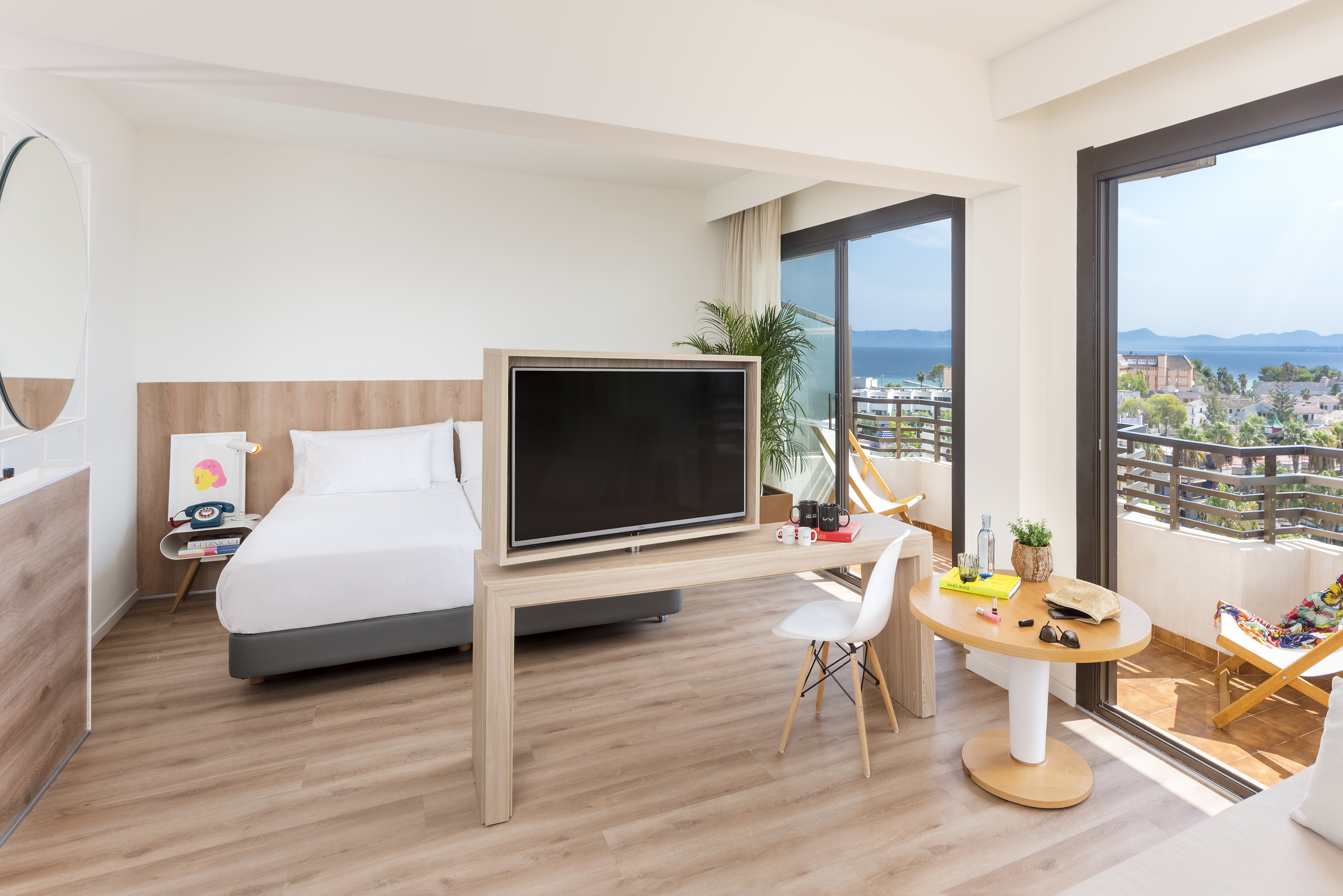 Modern hotel room with ocean view balcony, bed, TV, and light wood furniture.