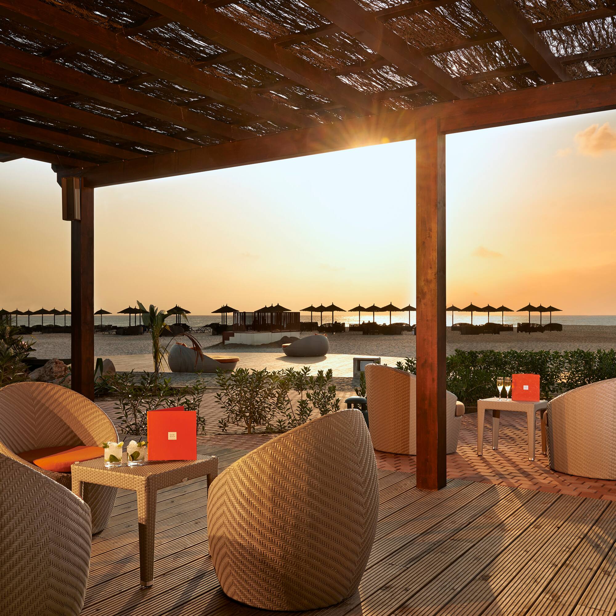 a patio with wicker chairs and tables on a beach