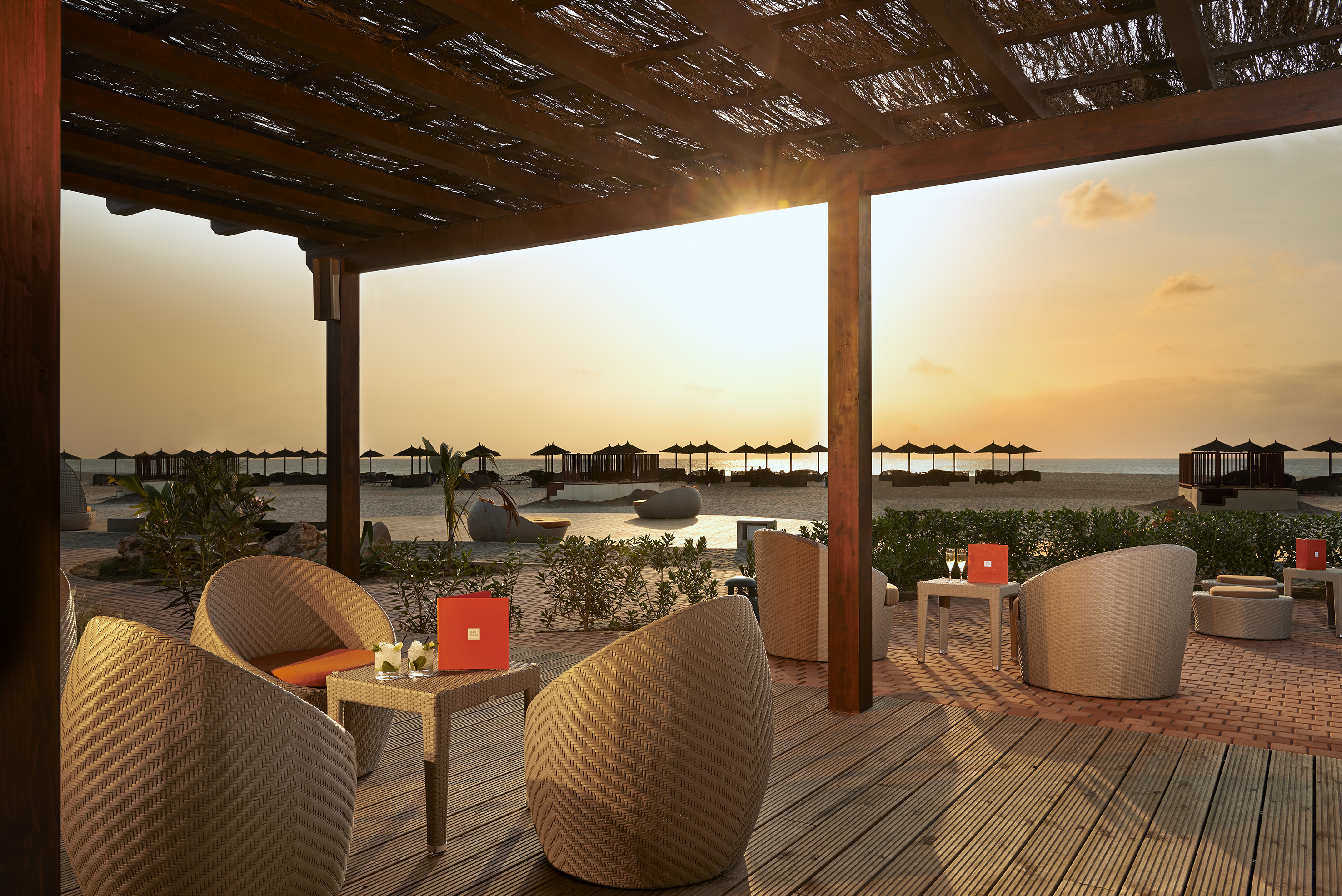 a patio with wicker chairs and tables on a beach
