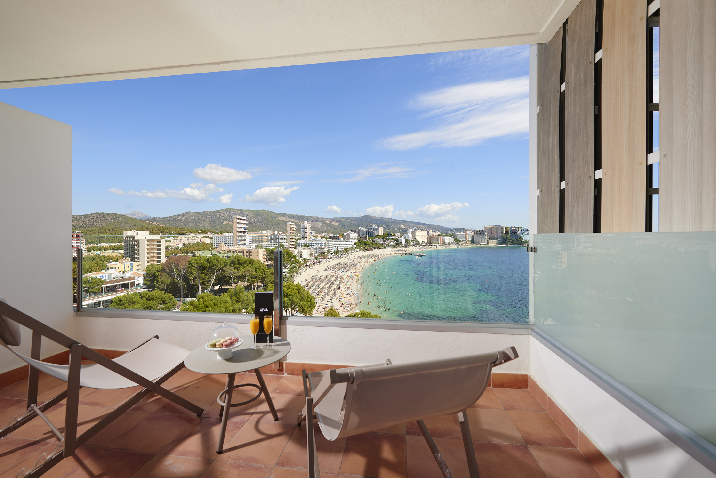 Balcony with sunny beach, turquoise sea, city, mountain views. Chairs & table.