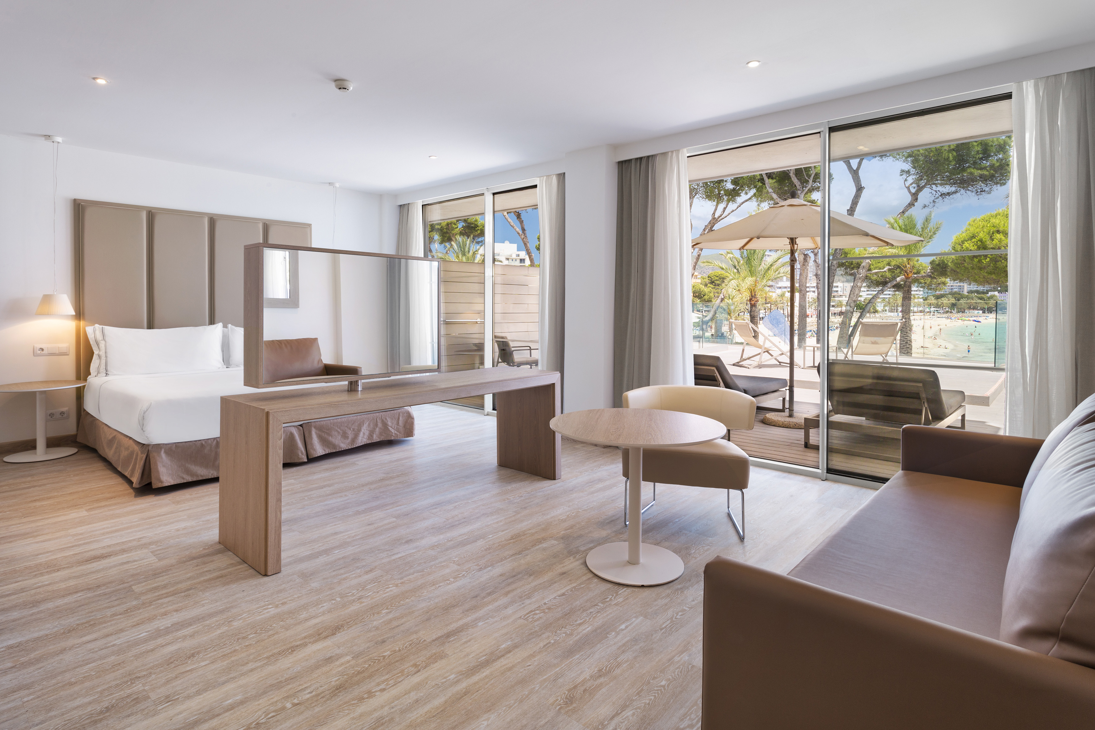 Modern beachfront hotel suite with balcony, bed, sofa, and ocean view.
