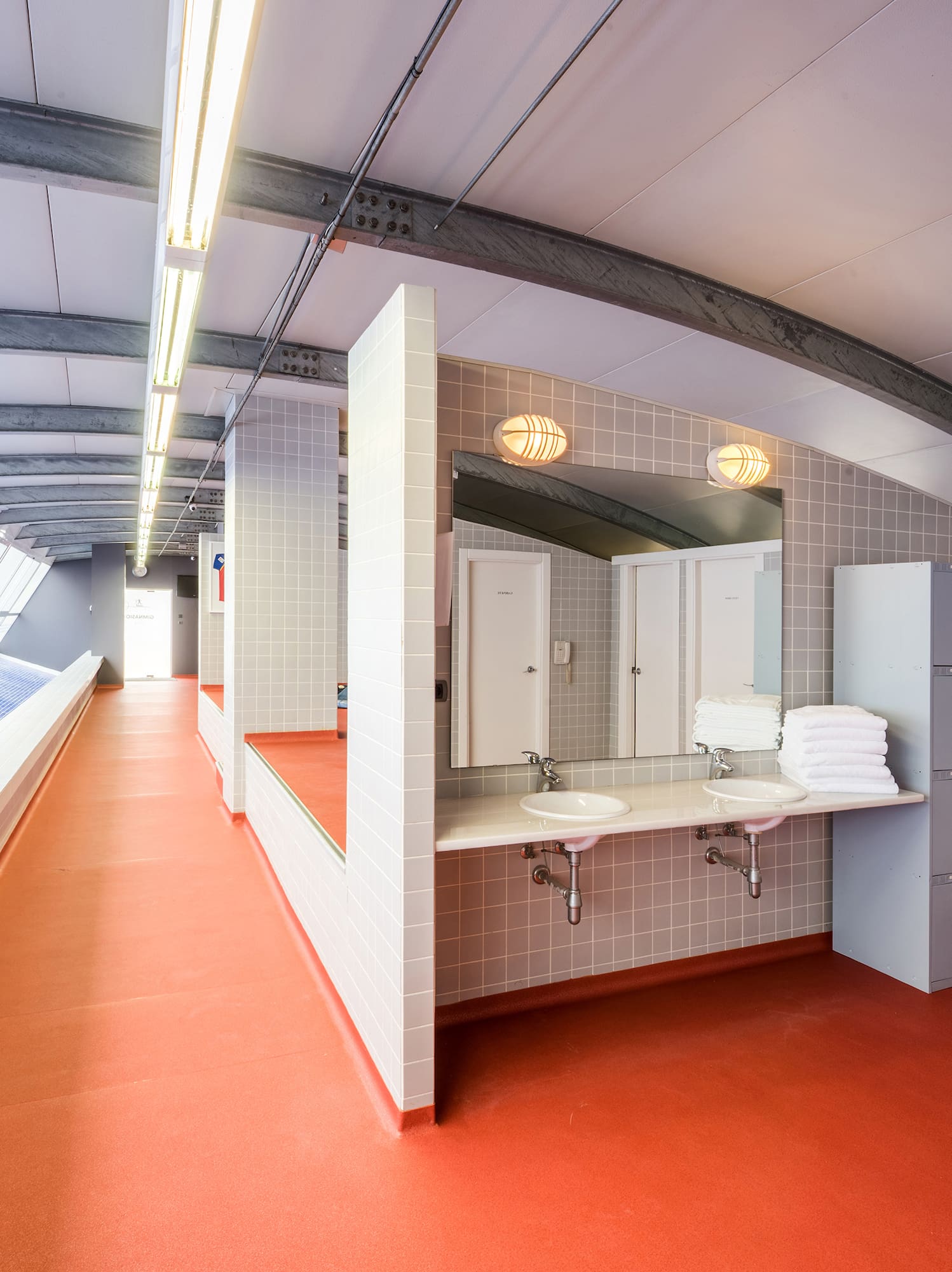 Vestuarios modernos con piscina interior, taquillas, lavabos y suelo rojo.
