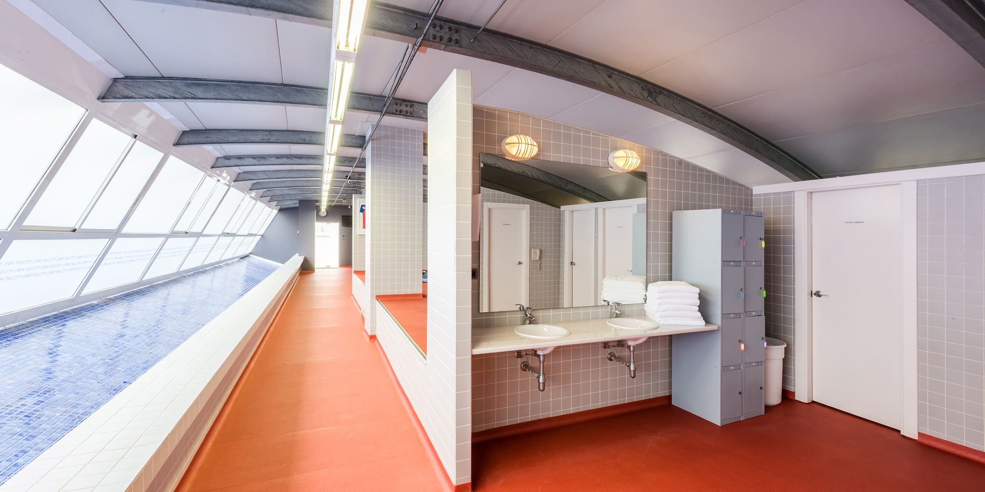 Modern changing room for indoor pool with red floor, sinks, and lockers.