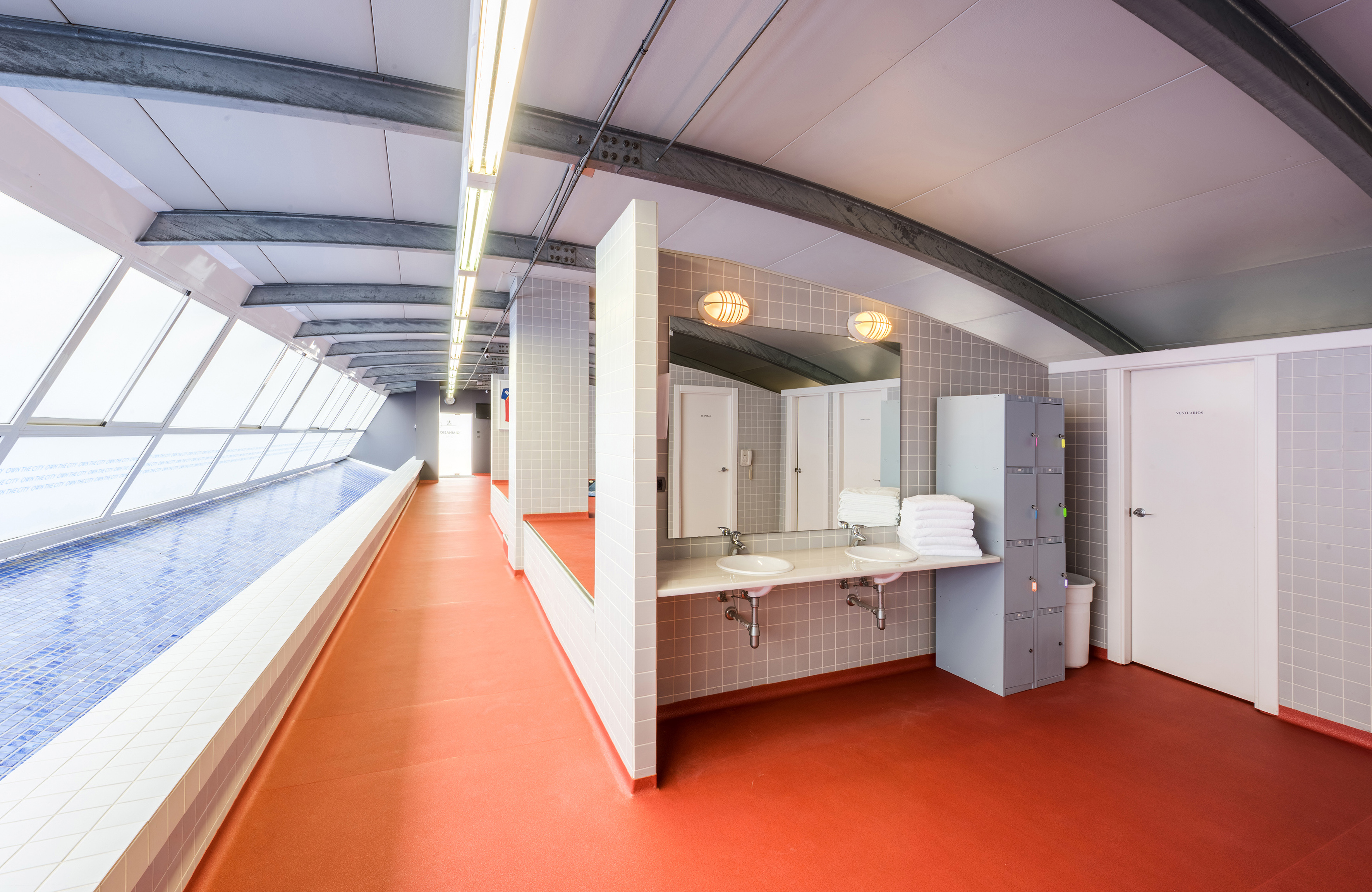 Vestuarios modernos con piscina interior, taquillas, lavabos y suelo rojo.