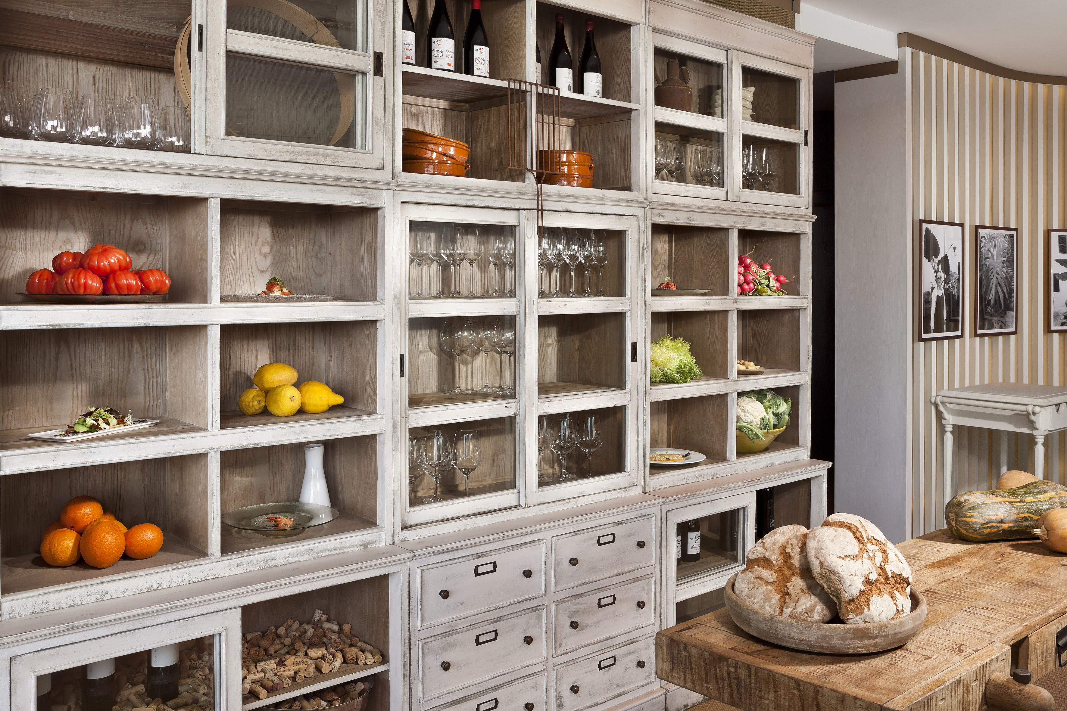Rustic white distressed kitchen cabinet with food, glassware, and wine display.