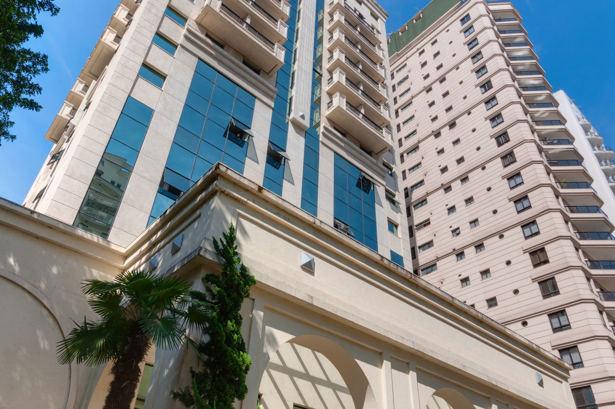 Light modern apartment building, glass facade, balconies, arched entrance, blue sky.