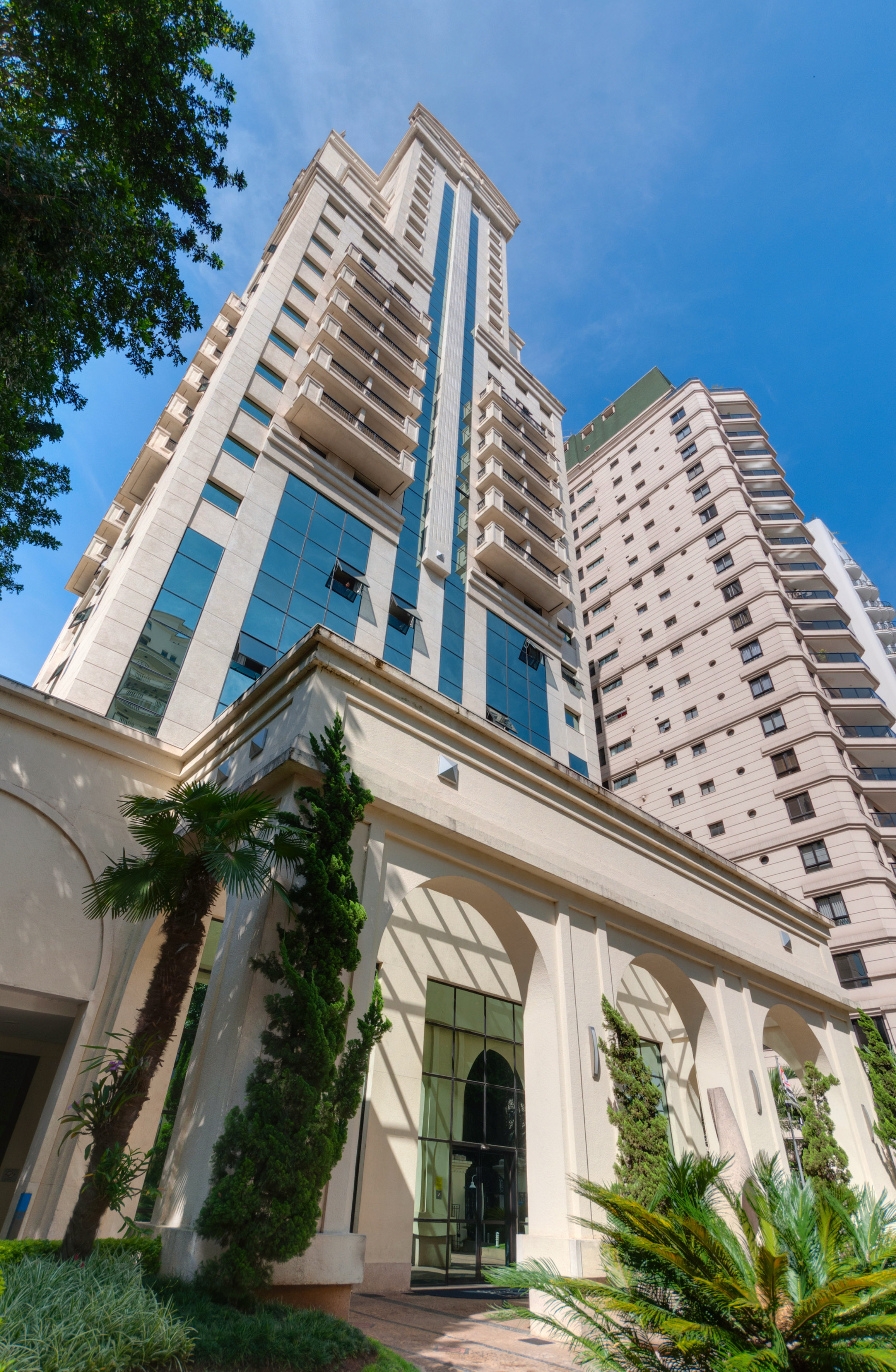 Light modern apartment building, glass facade, balconies, arched entrance, blue sky.
