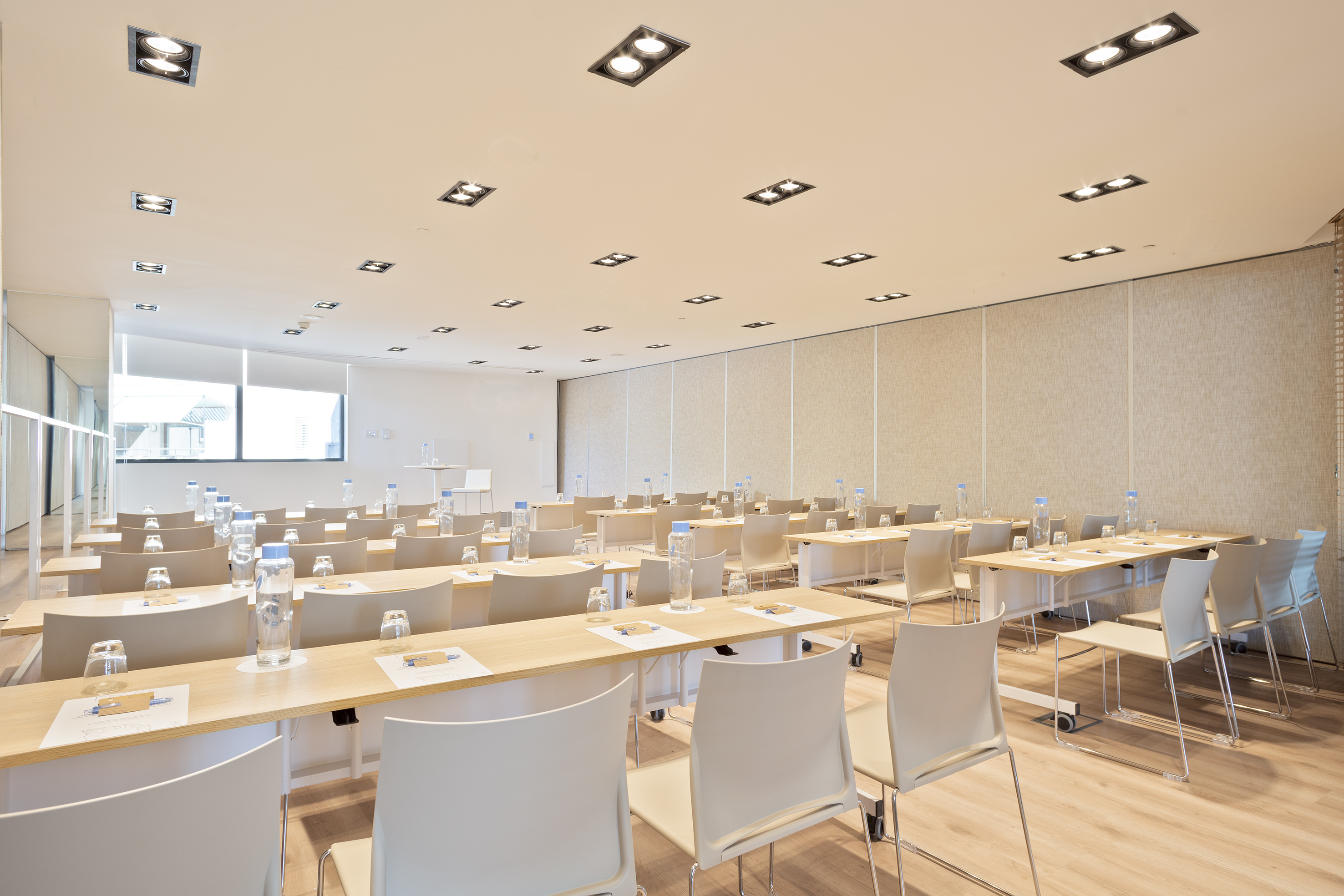 Modern empty conference room with classroom setup, tables, and water bottles.