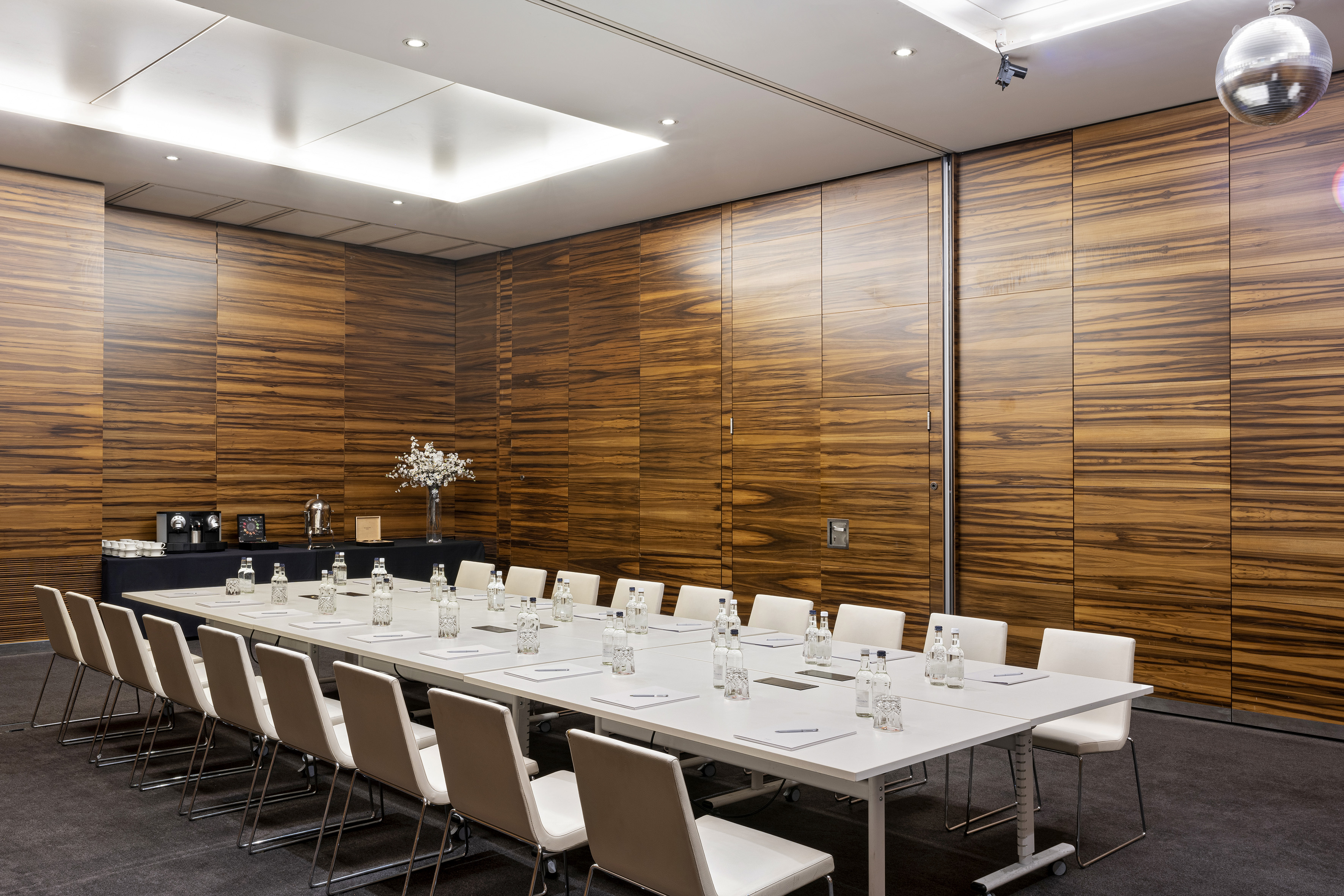 Modern conference room with long white table, chairs, and distinct wood panel walls.