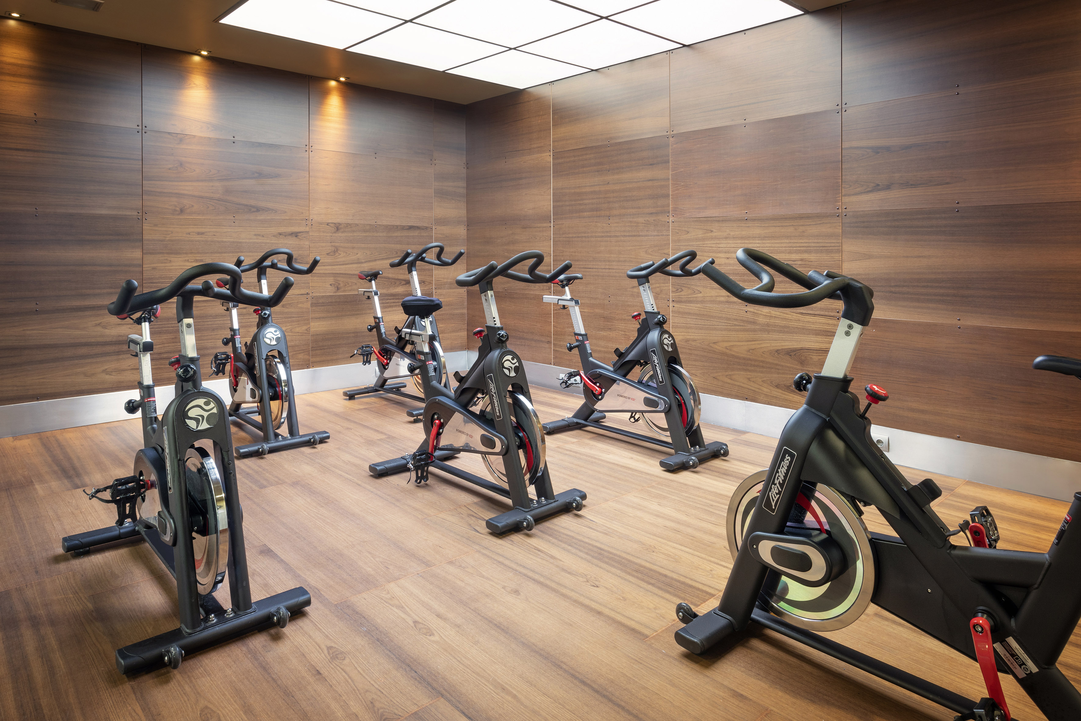 Spin bikes in a modern gym studio with warm wood walls and floor.