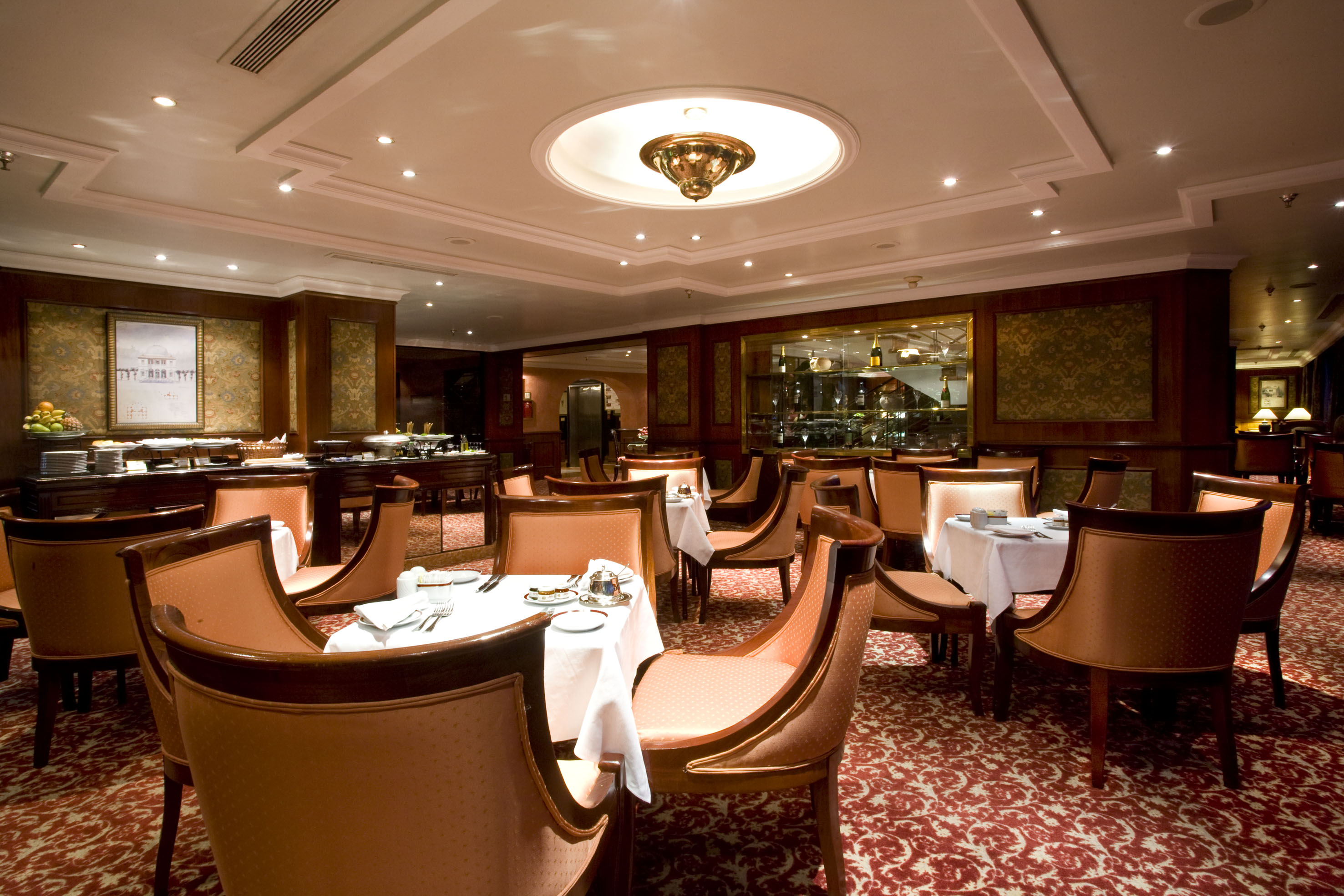 Luxury hotel restaurant interior with formal tables, red carpet, and buffet.