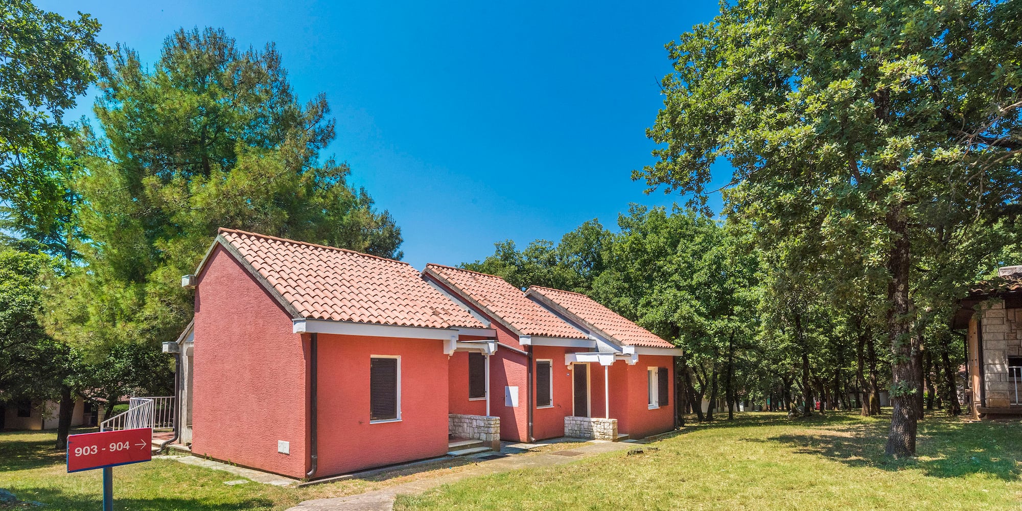 a two red houses with a lawn and trees in the background