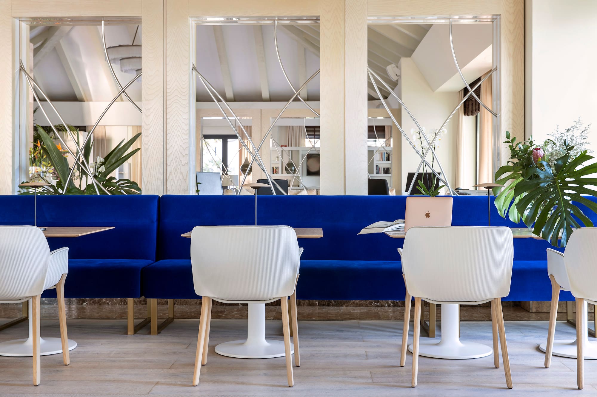 Blue velvet sofa, white chairs, mirrored wall in modern hotel lounge.