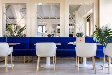 a blue couch with white chairs and tables in a room with mirrors