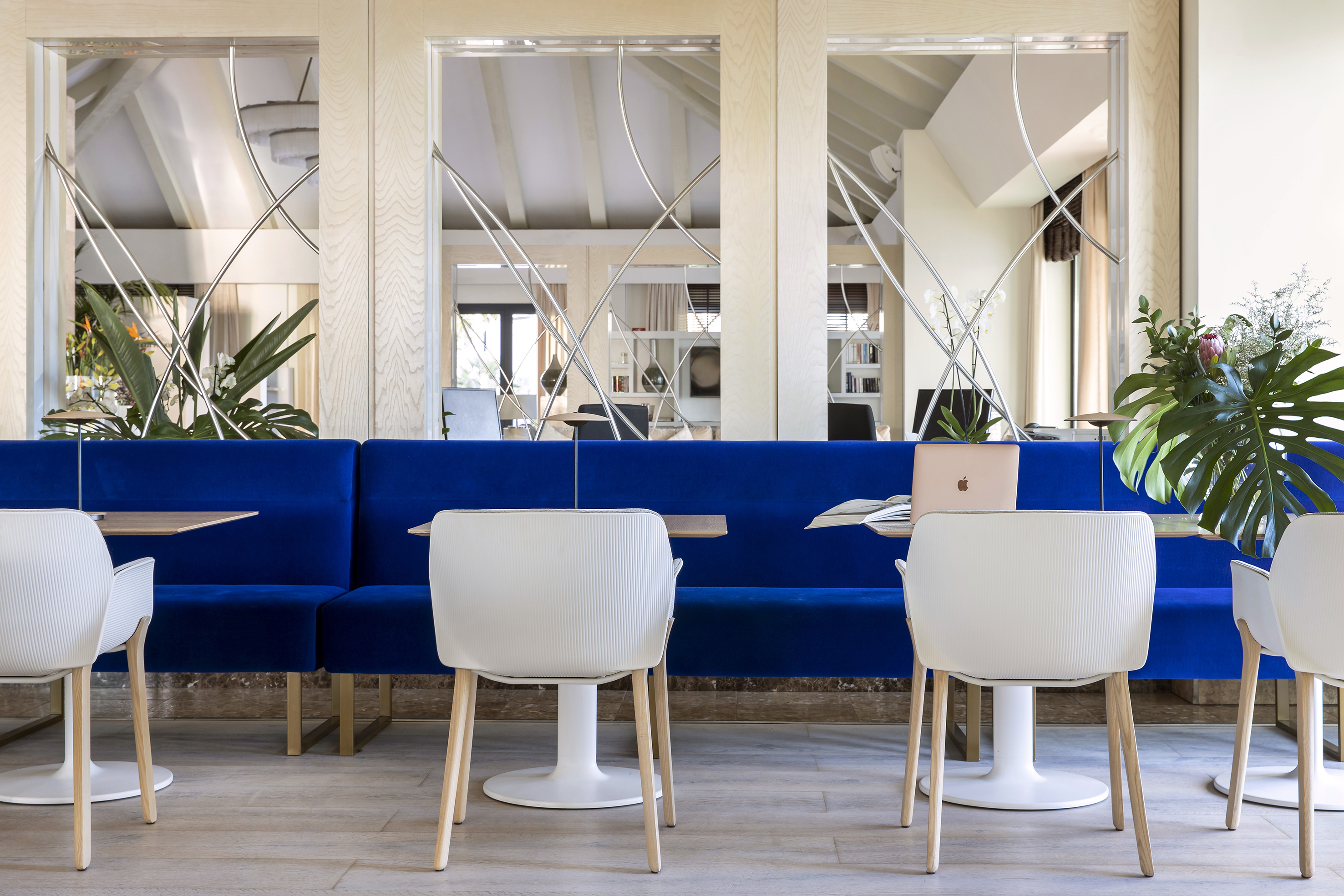 a blue couch with white chairs and tables in a room with mirrors