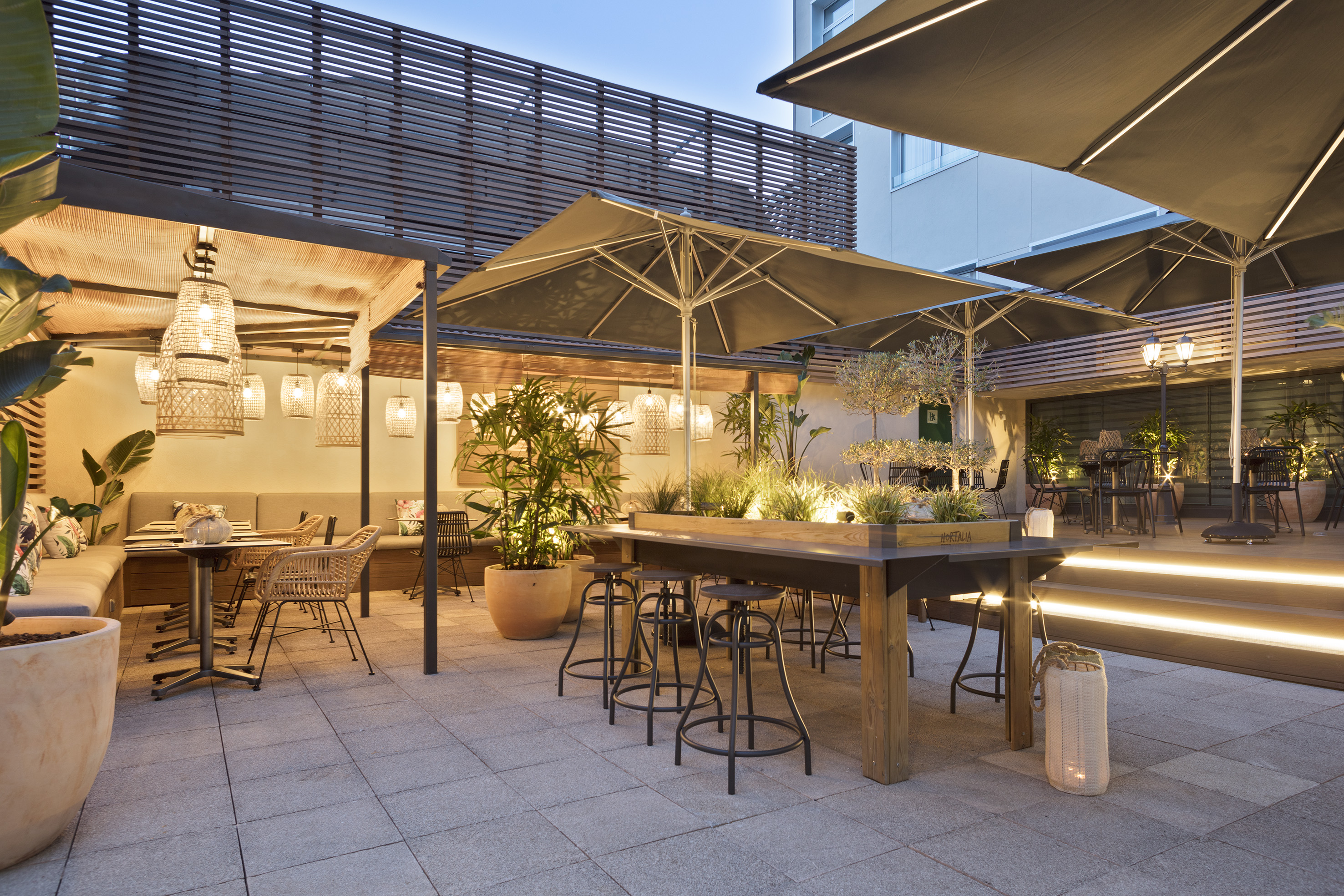 Chic outdoor dining terrace with modern seating, ambient lights, and green plants.
