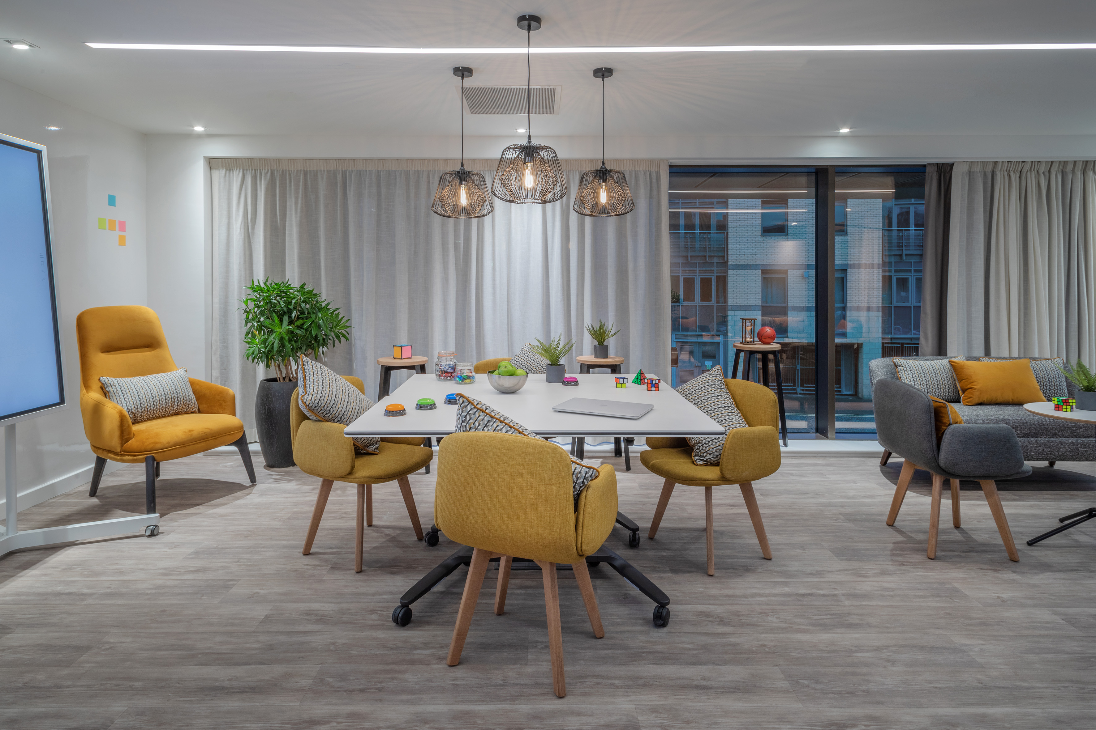 Modern collaboration room with yellow chairs, white table, and lounge area.