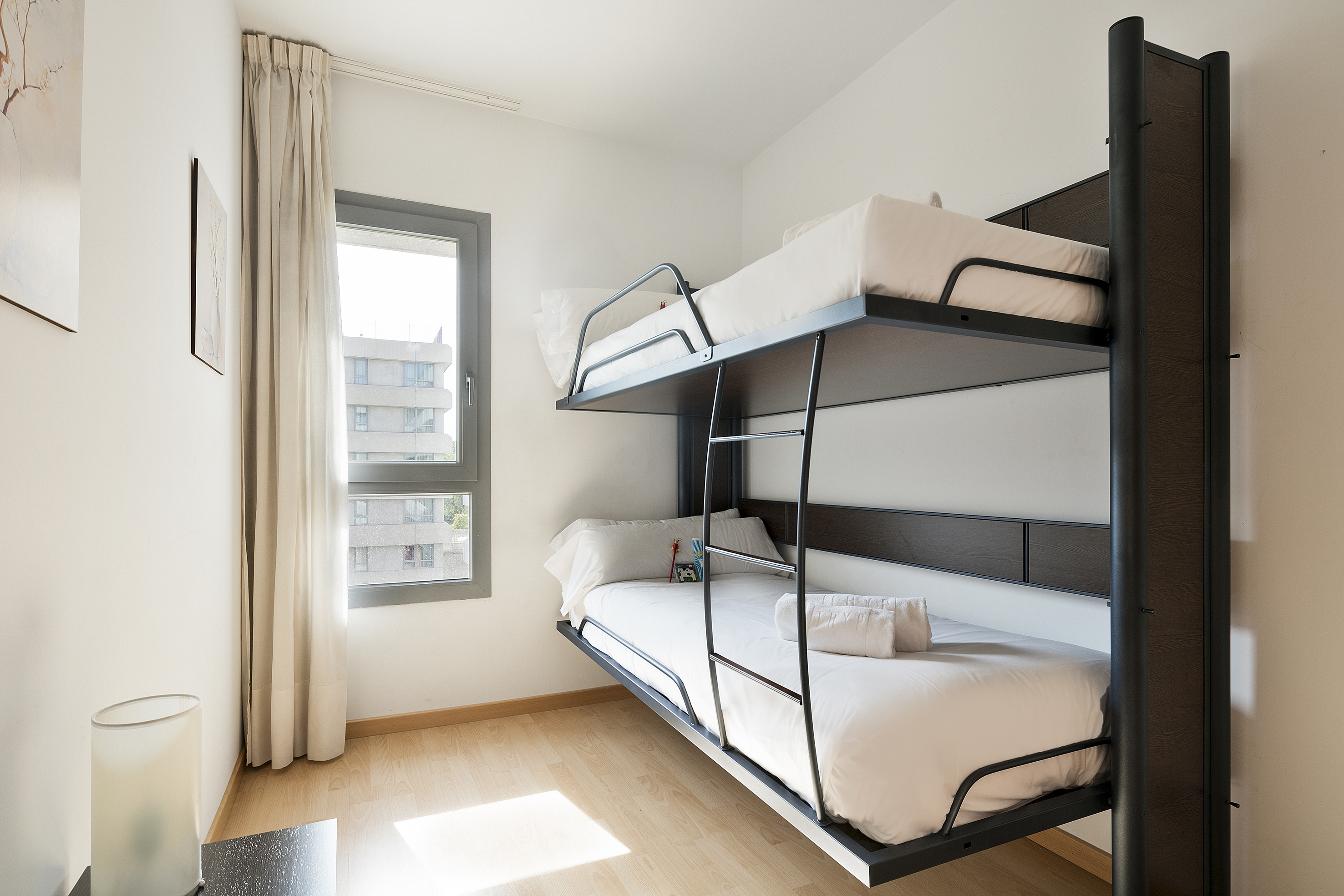 Bright bedroom with modern bunk bed, white linens, wooden floor, and window.