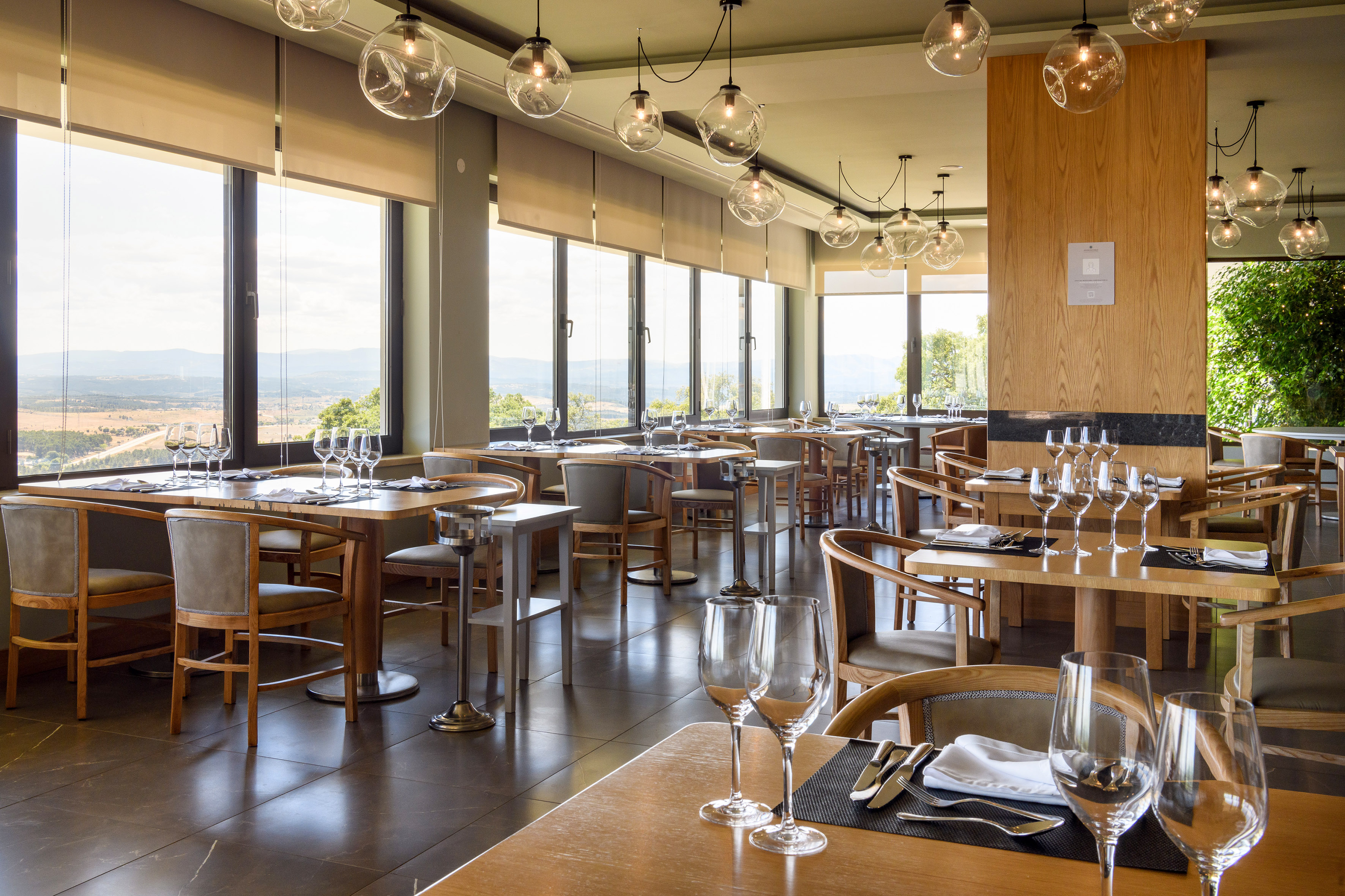 Restaurant interior with set tables, large windows overlooking a scenic landscape.