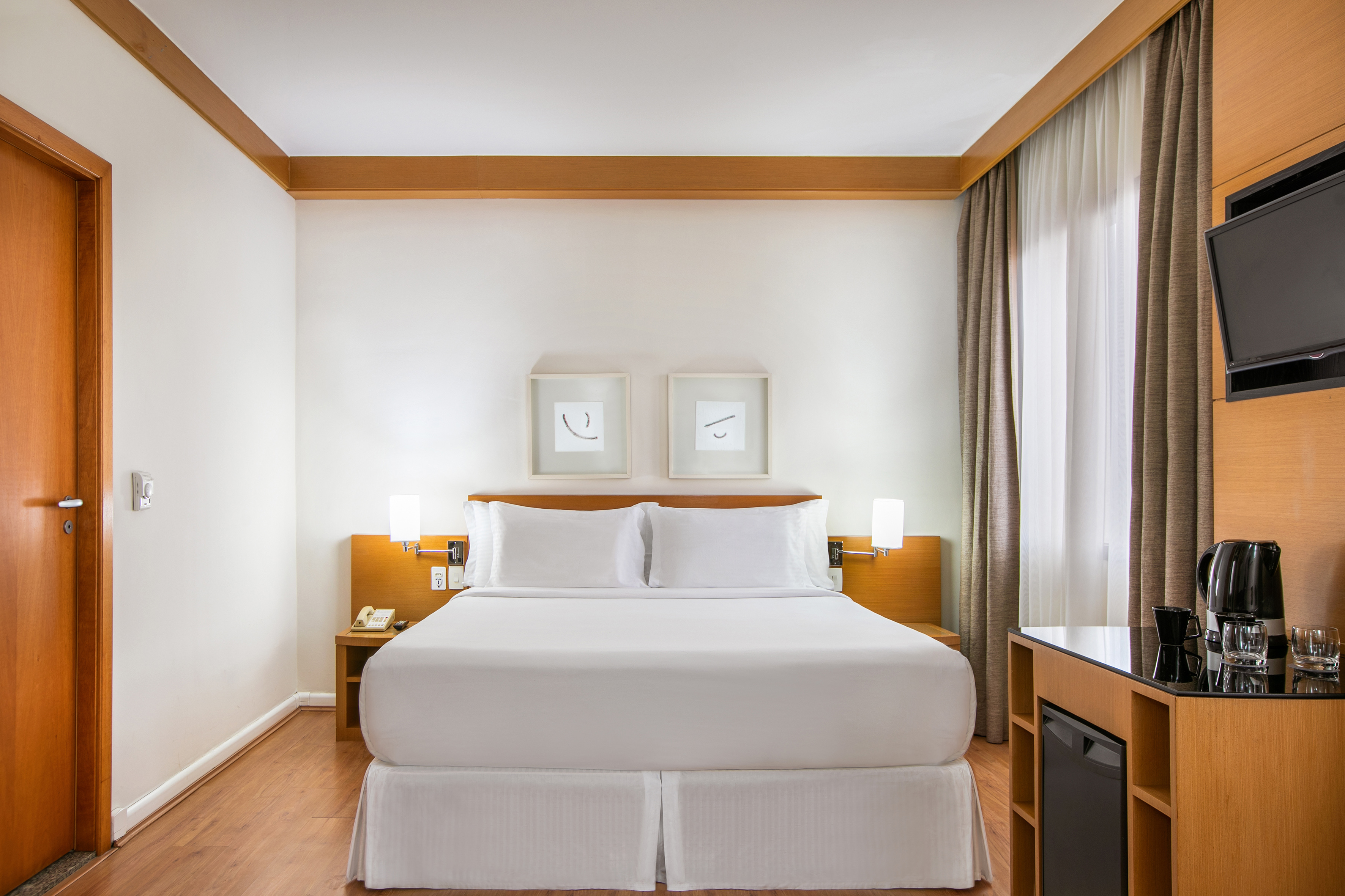 Modern hotel room with queen bed, white linen, and wooden furniture.