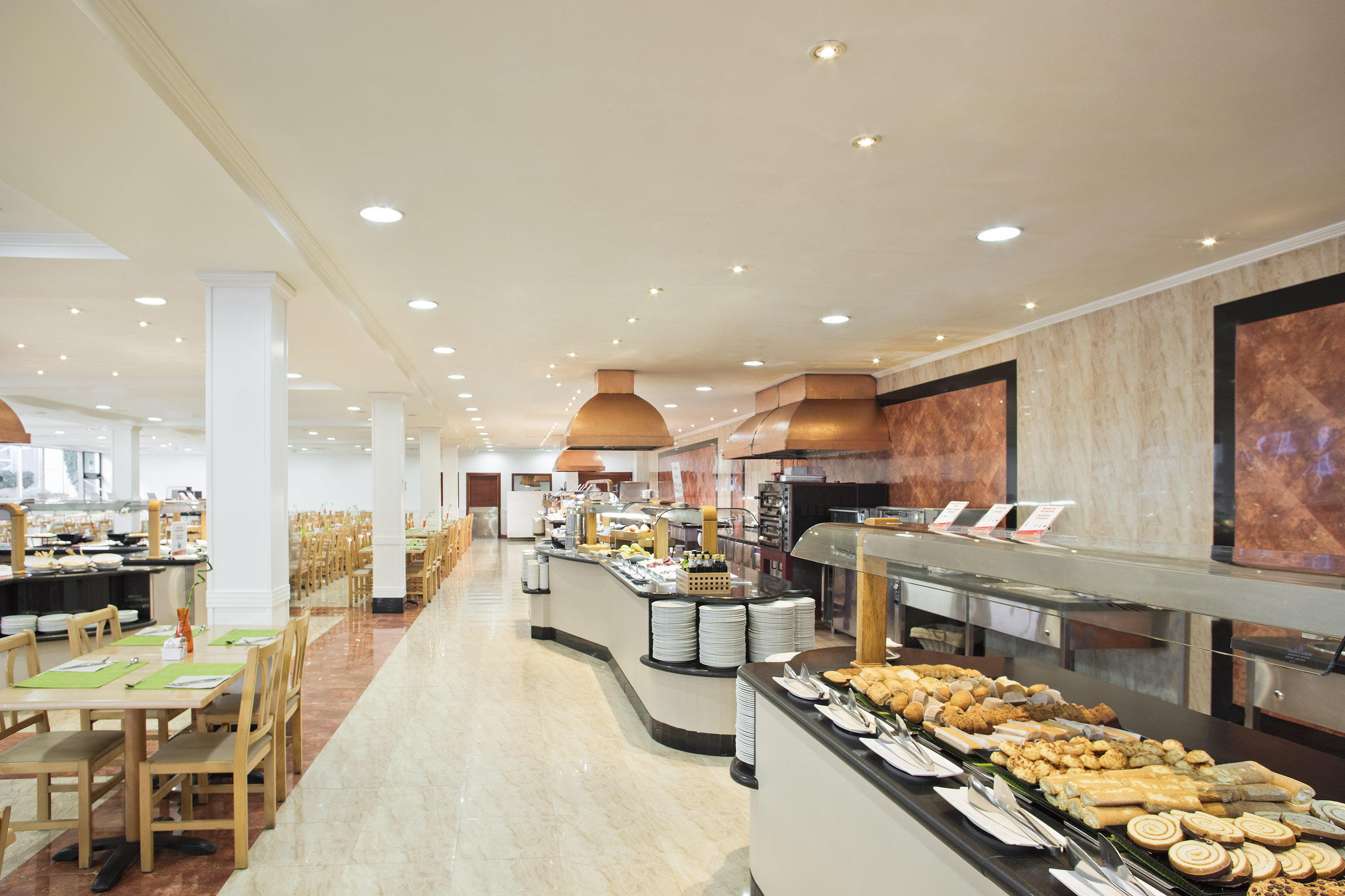 Bright hotel buffet restaurant with pastry counter and dining tables.