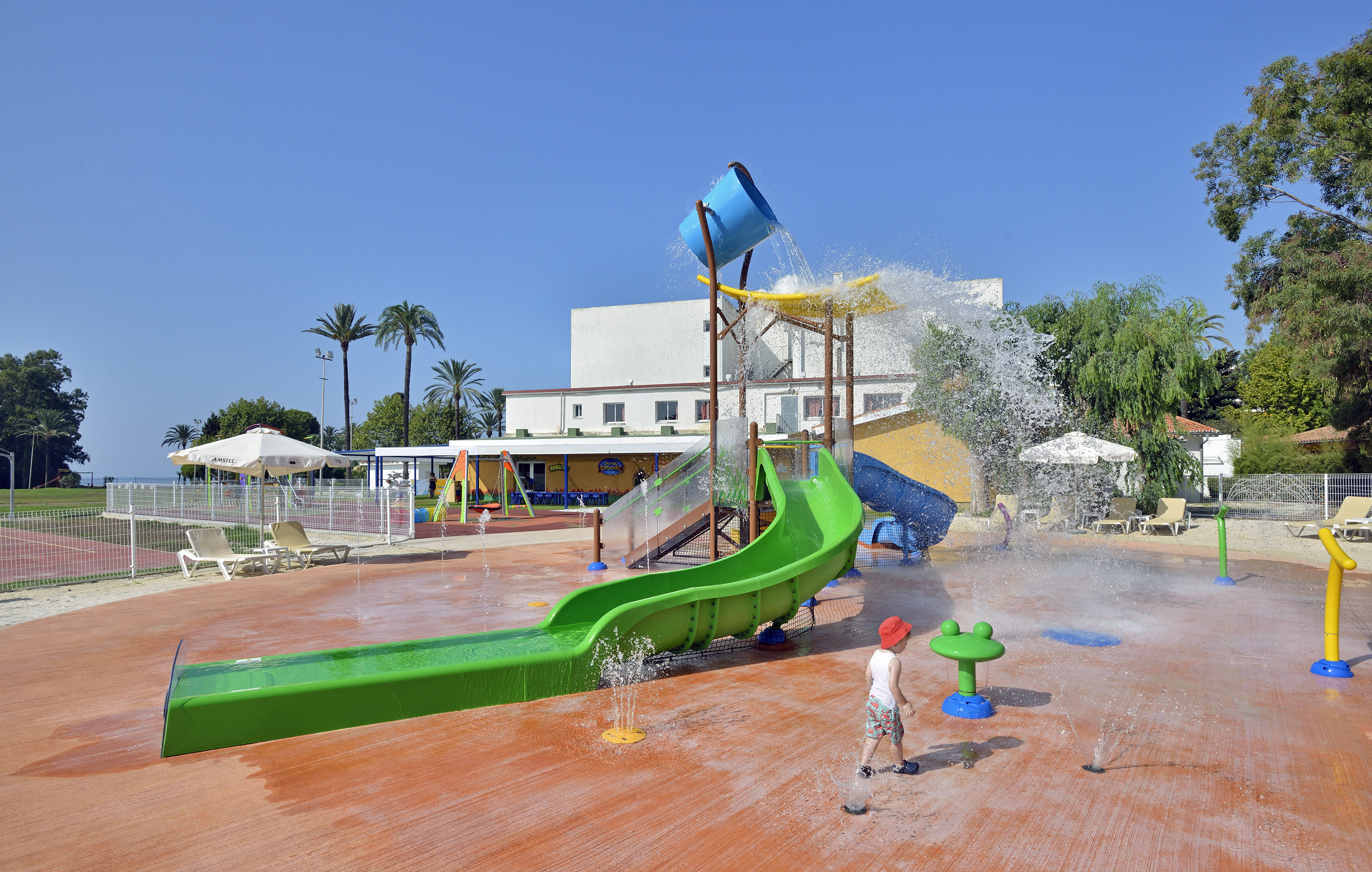 Kids water park splash pad with green slide, tipping bucket, and child playing.