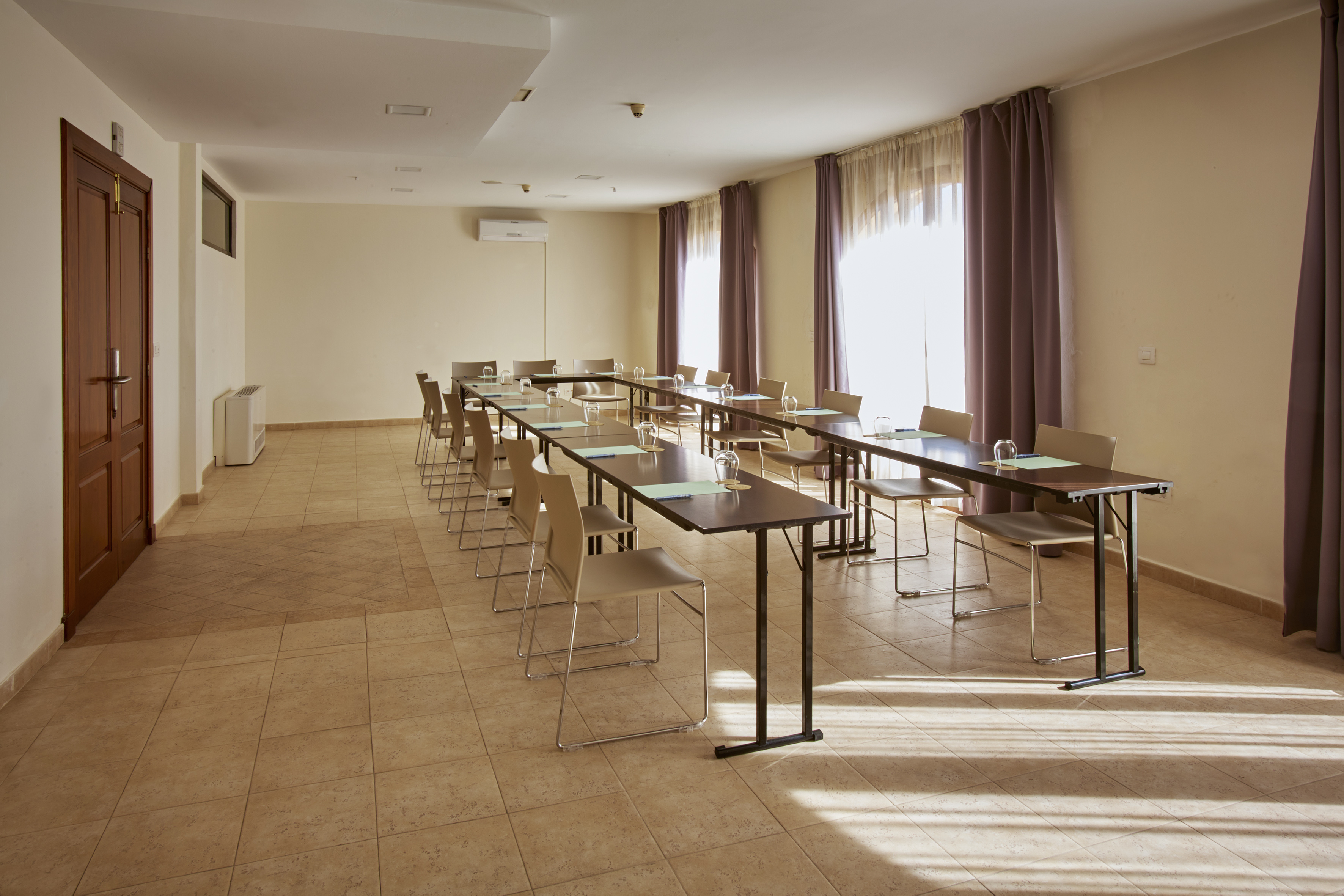 Bright conference room with U-shaped tables, chairs, and natural light from windows.