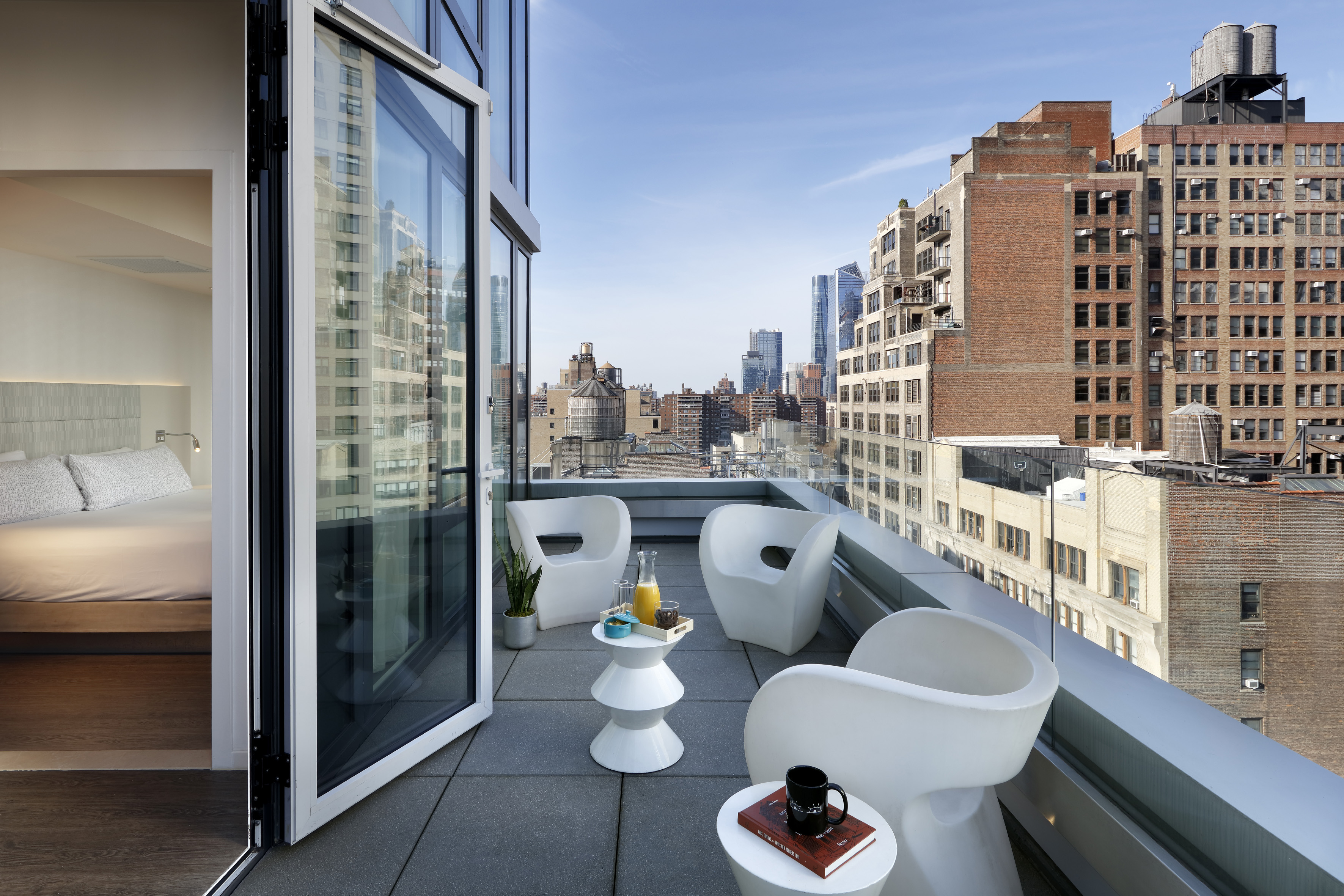 Urban hotel balcony with modern white furniture and city skyline view.