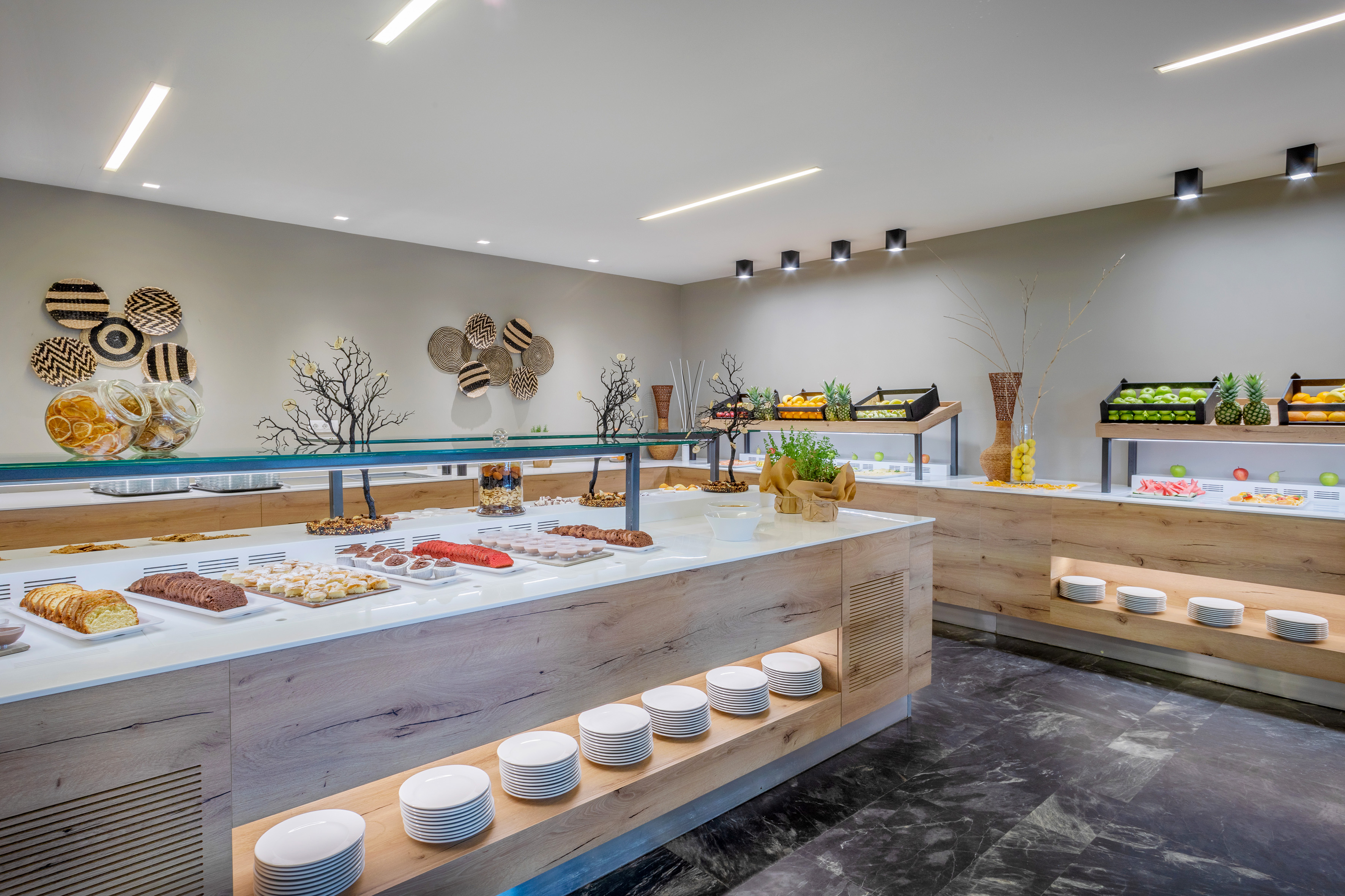 Hotel buffet with fresh fruit, pastries, bread in a modern dining area.