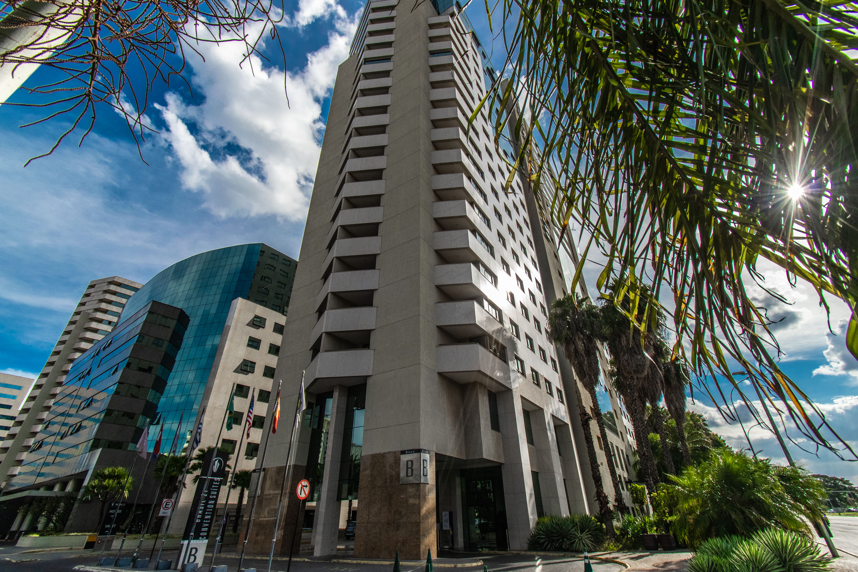 Modern hotel and convention center buildings with glass facades, palm trees, sunny sky.