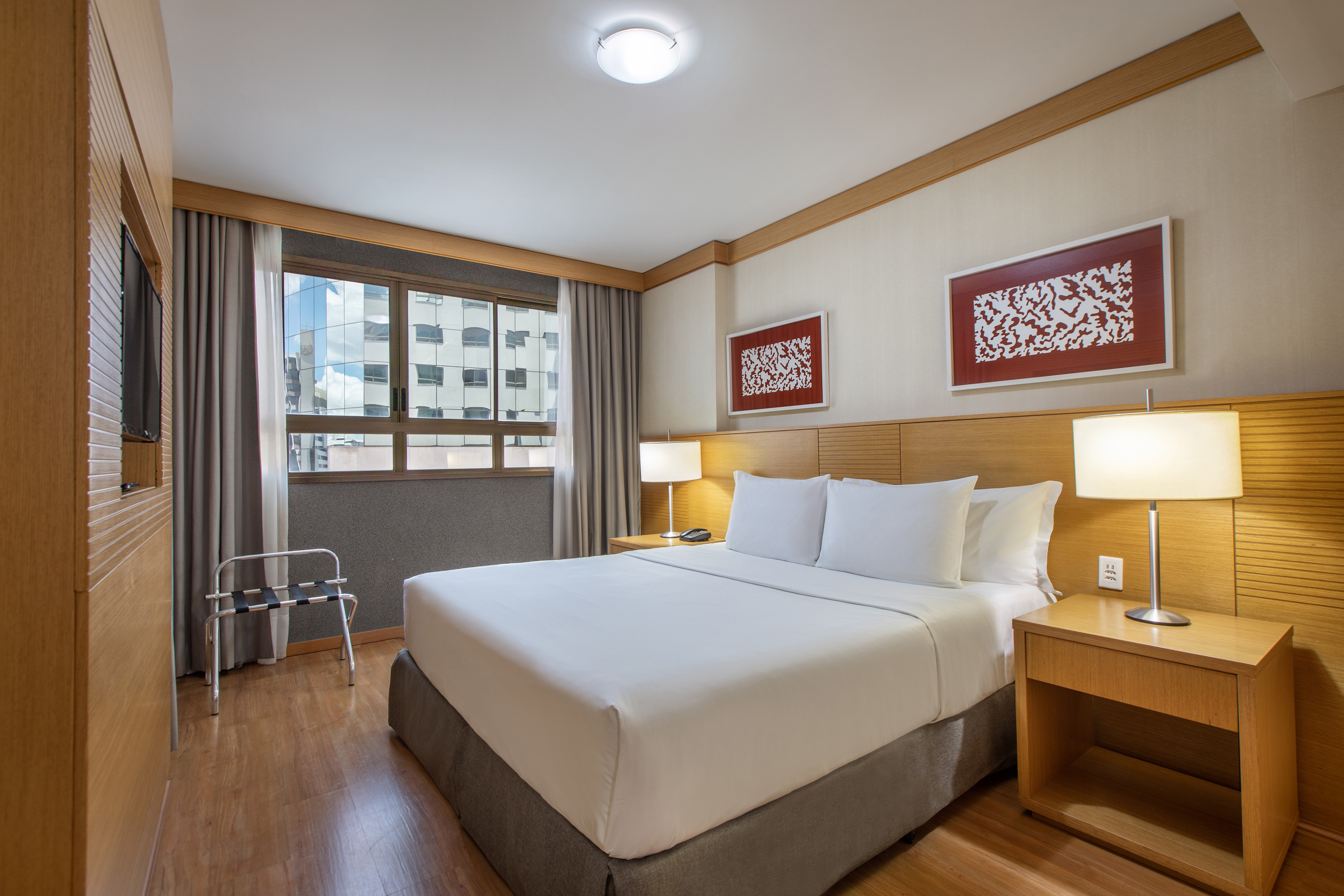 Modern hotel room with king bed, wooden accents, and city view window.