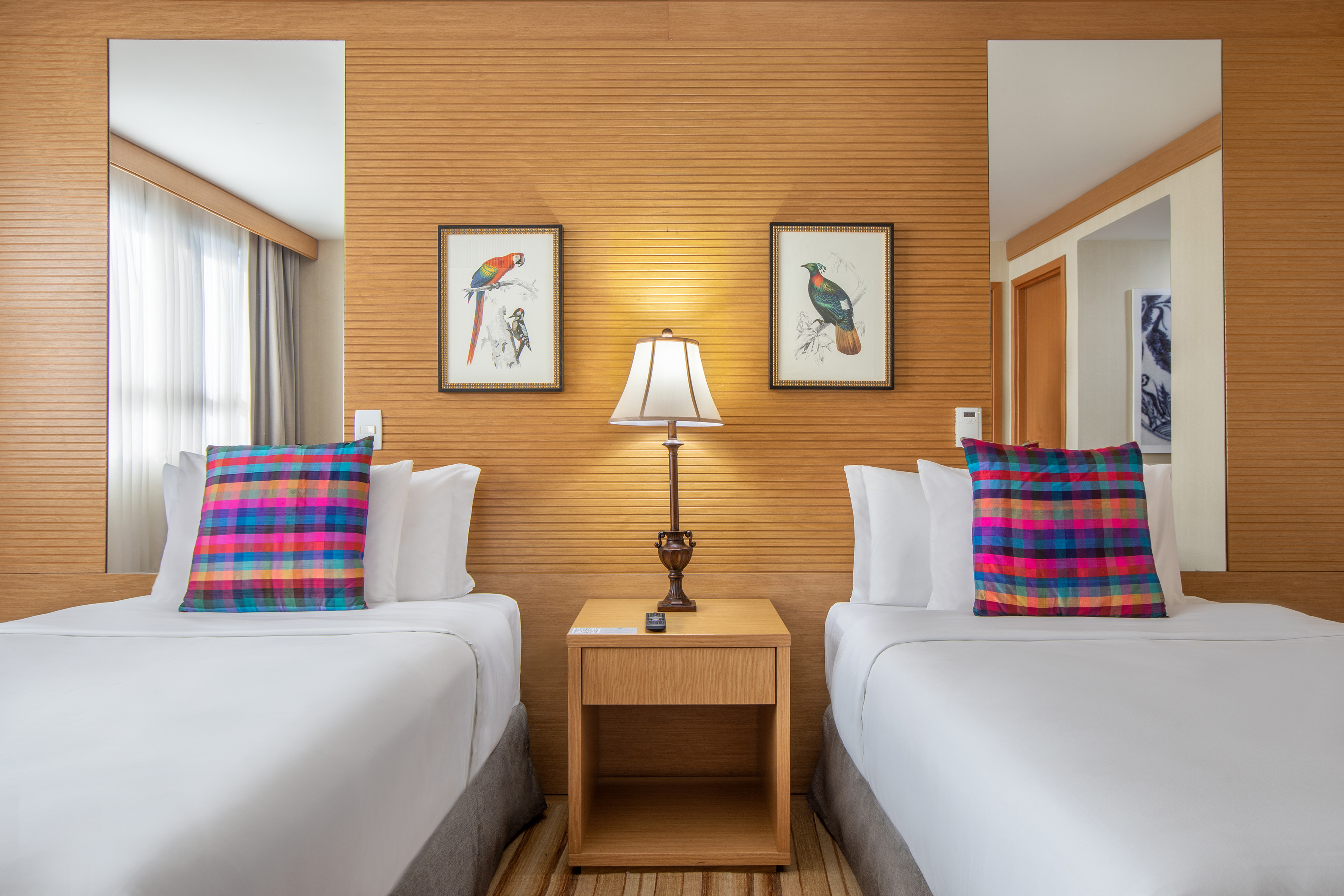 Modern twin bed hotel room with colorful pillows and wooden headboard.