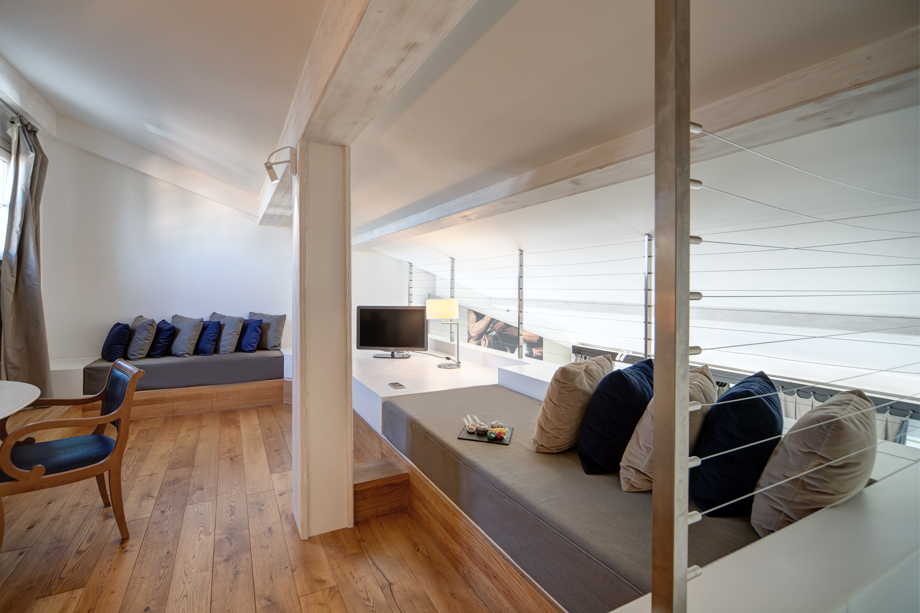 Bright modern loft suite with wooden beams, cozy seating, and hardwood floor.
