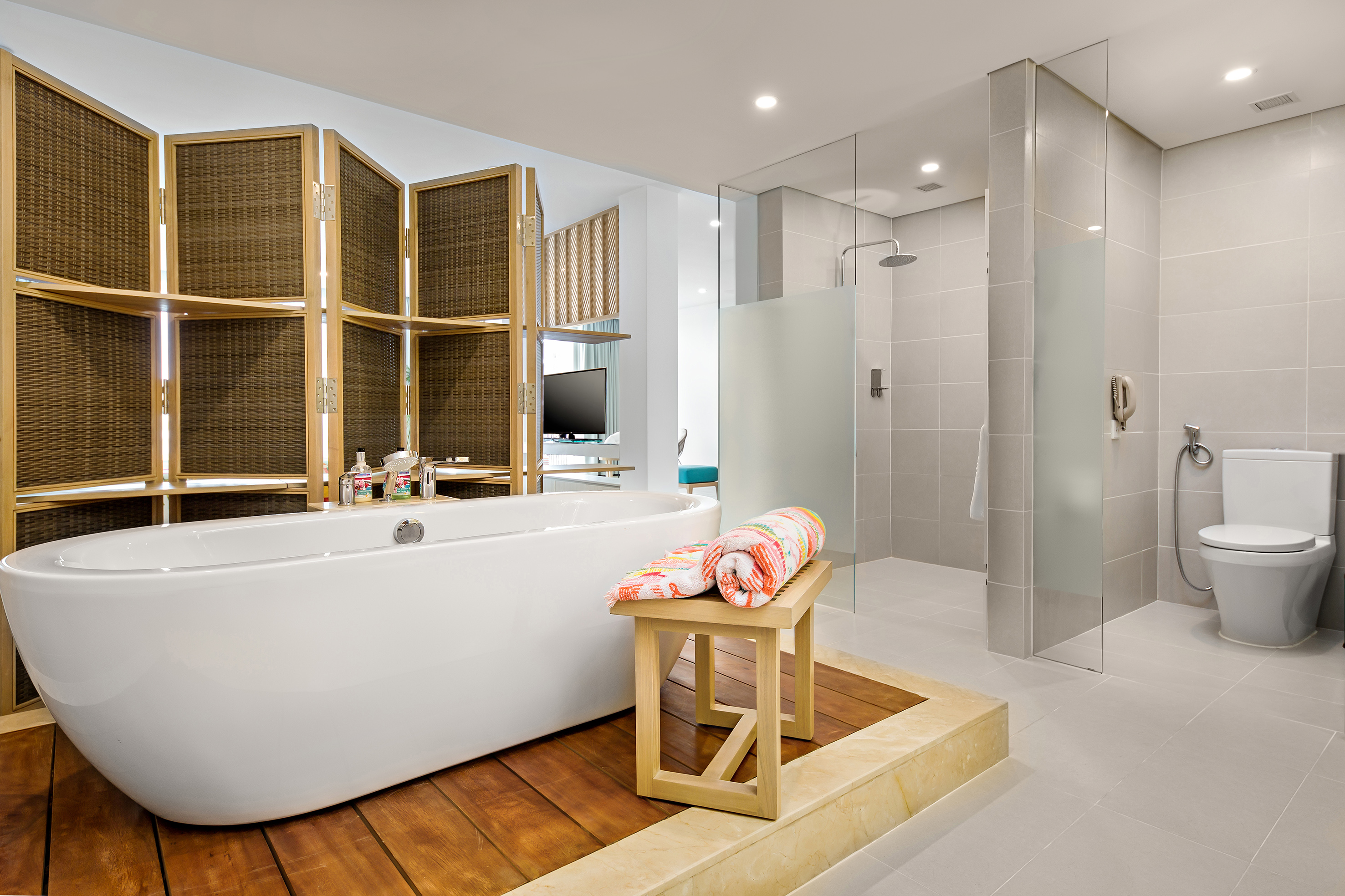 Hotel bathroom with freestanding tub, wooden divider screen, and glass shower.