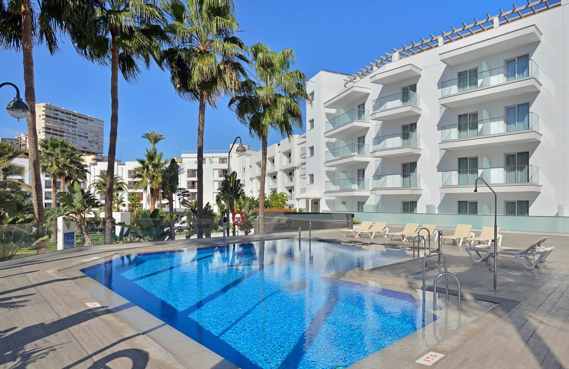 Outdoor pool with lounge chairs and palm trees near a modern white building.