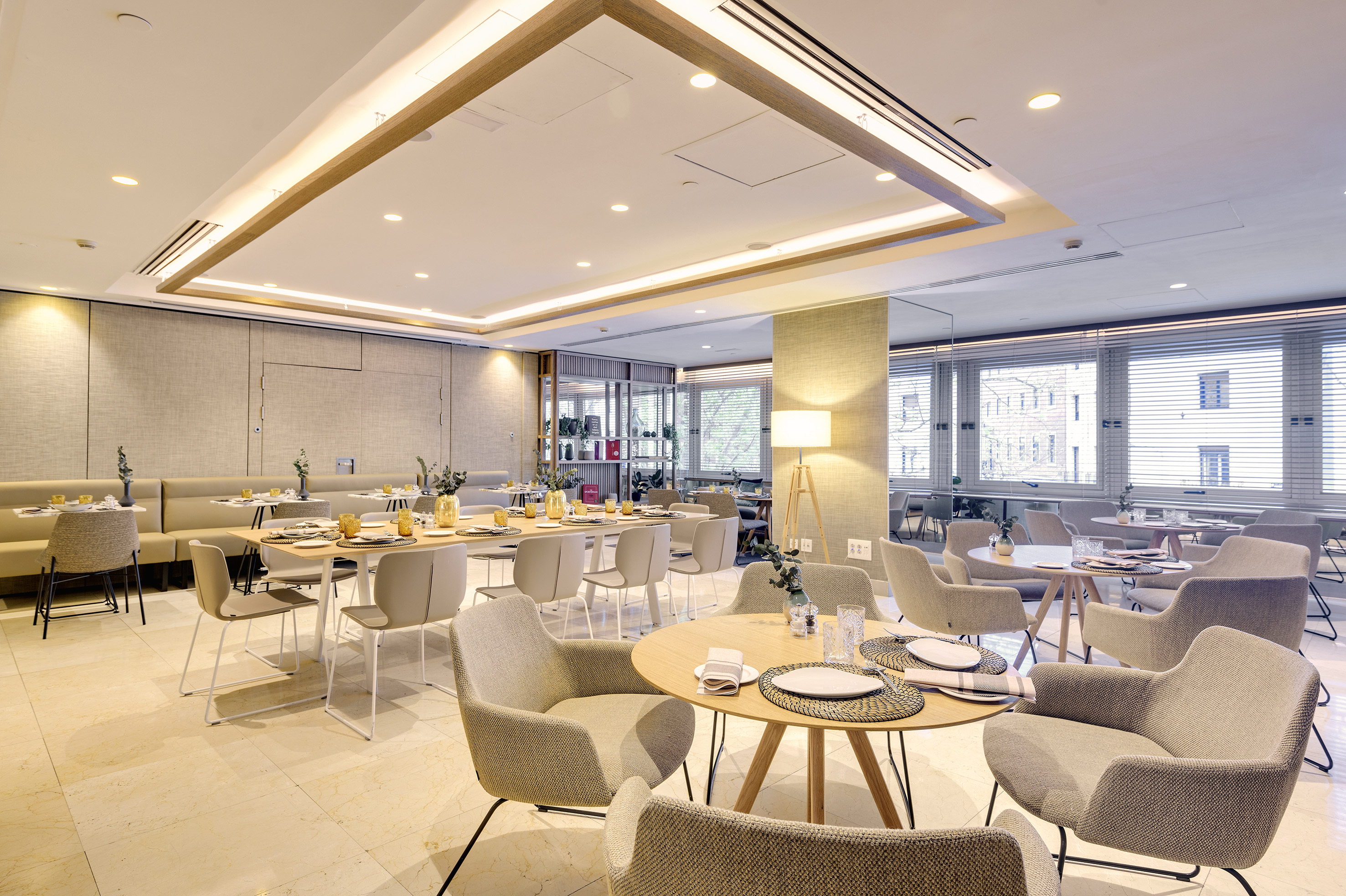 Modern dining room with beige chairs, set tables, and windows with blinds.
