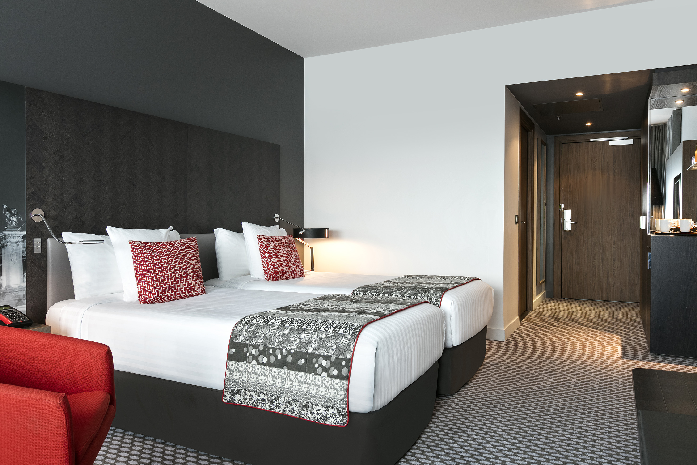 Stylish hotel bedroom featuring twin beds, red armchair, and patterned bedding.