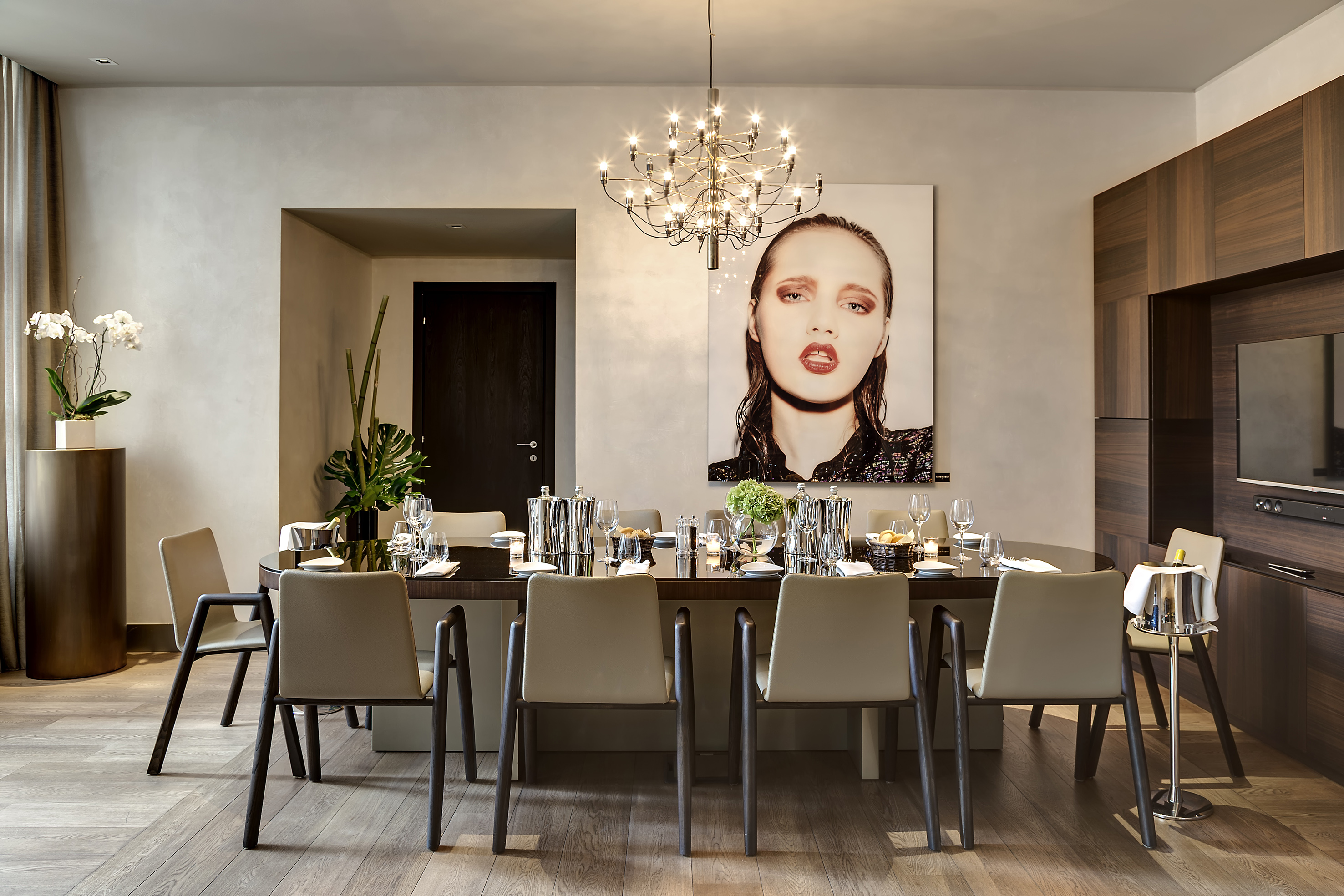 Modern dining room with oval table, chairs, chandelier, and bold art.